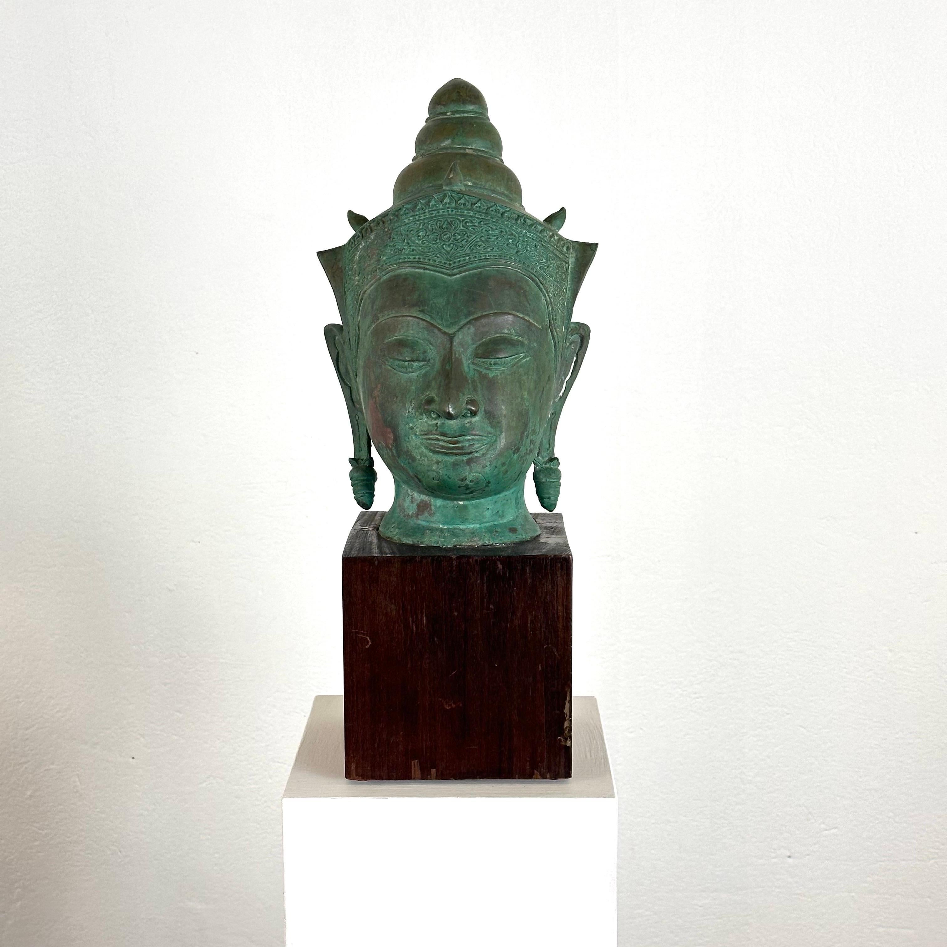 Immerse yourself in the serene beauty of Thai craftsmanship with this magnificent 19th-century bronze Buddha head, elegantly presented on a wooden base. Radiating an aura of timeless tranquility, this piece captivates with its exquisite patina and