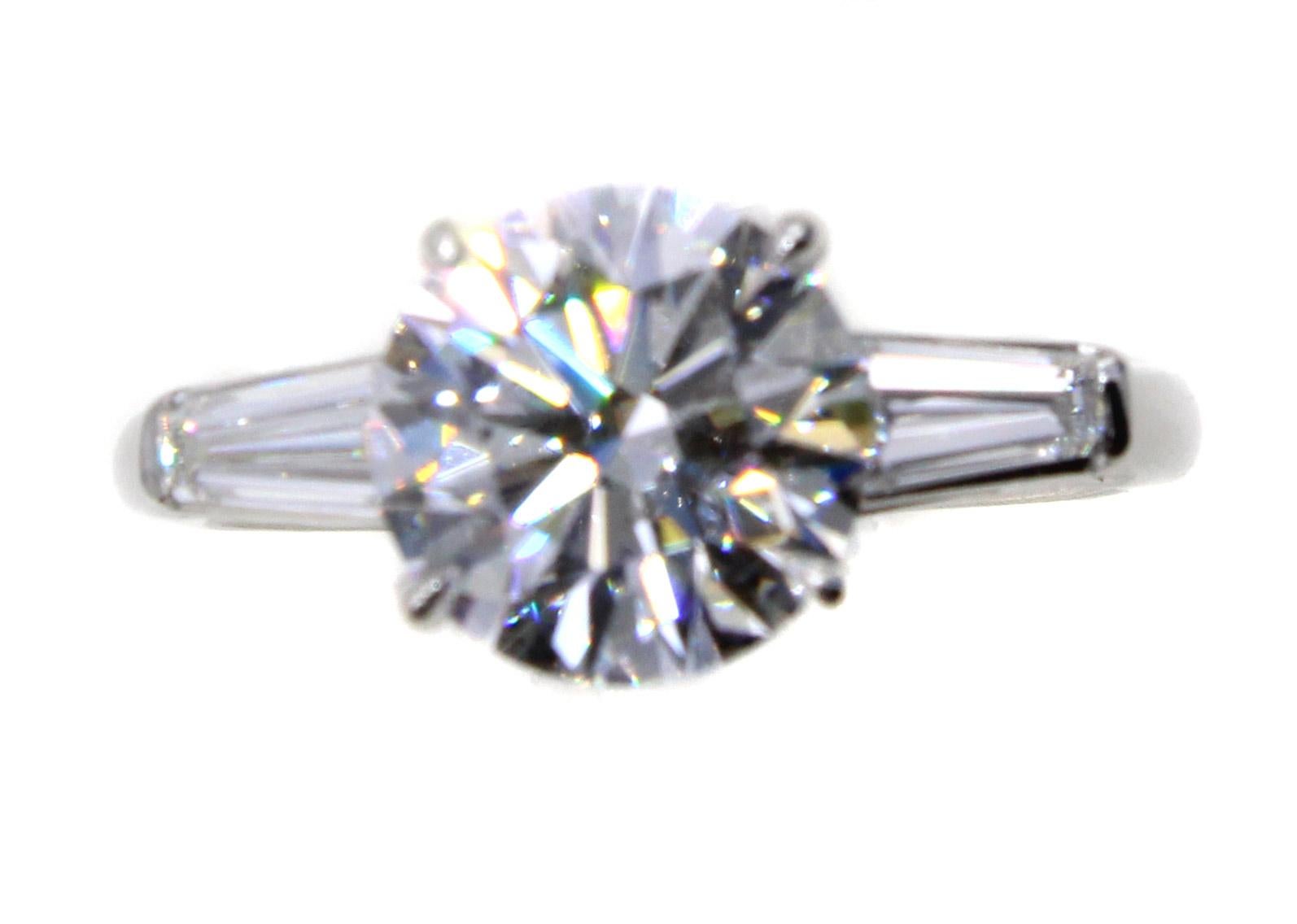 Le diamant parfait, un brillant rond pesant 2,56 carats, de couleur et de clarté D et IF (internally flawless), est serti dans une bague classique en platine faite à la main avec deux baguettes effilées sur le haut des branches. La taille, le