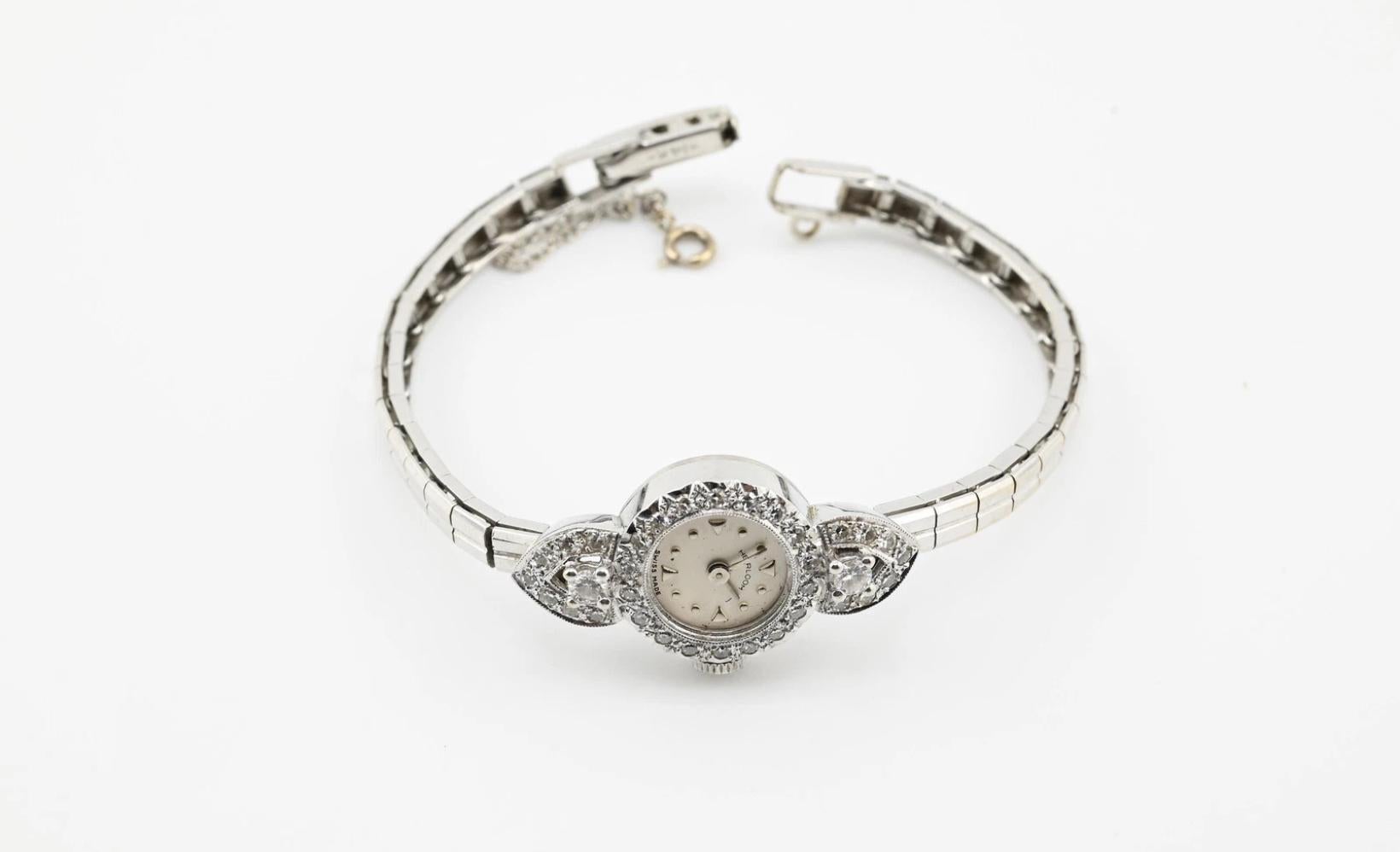 Questo orologio da cocktail da donna Art Deco mozzafiato è uno splendido esempio di eleganza e maestria artigianale dei primi del Novecento. Realizzato in lussuoso oro bianco 14 carati, l'orologio presenta un design intricato ornato da diamanti