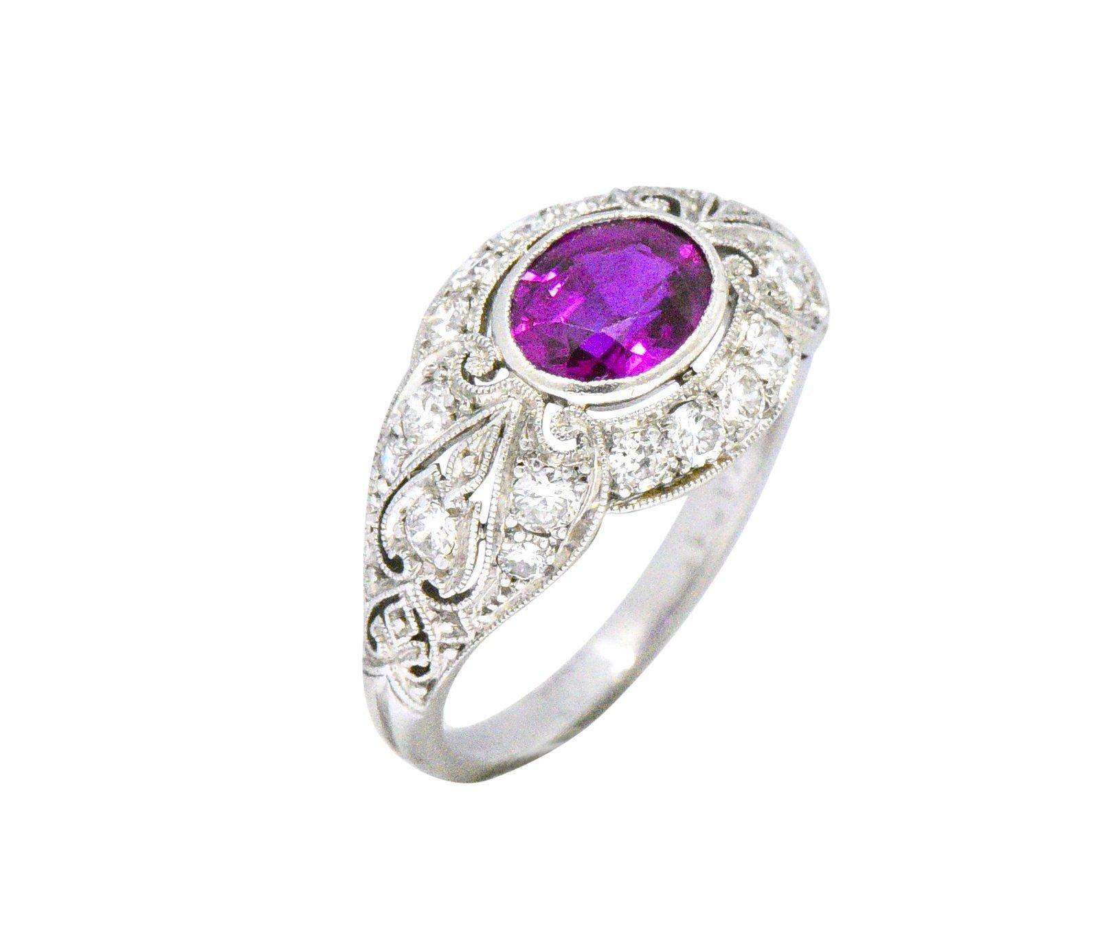 Centering an oval cut pink Burma sapphire weighing 1.02 carats, saturated in color with no evidence of heat

Bezel set in a scrolled mounting with milgrain edge detail and fluer-de-lis shoulder motif

Accented throughout by old European cut diamonds