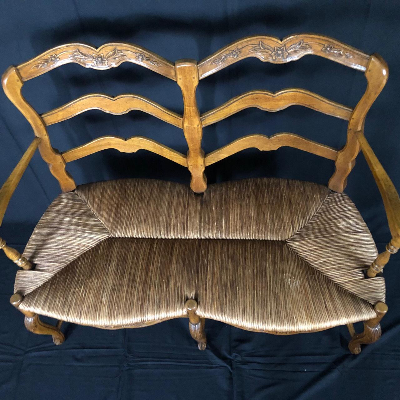 An exquisitely carved walnut ladderback bench from 19th century France having graceful curved arms with inset detail and subtle cabriole legs with acanthus leaves on knees and top. Intricate carving on stretcher, apron and top of backrest. Marvelous