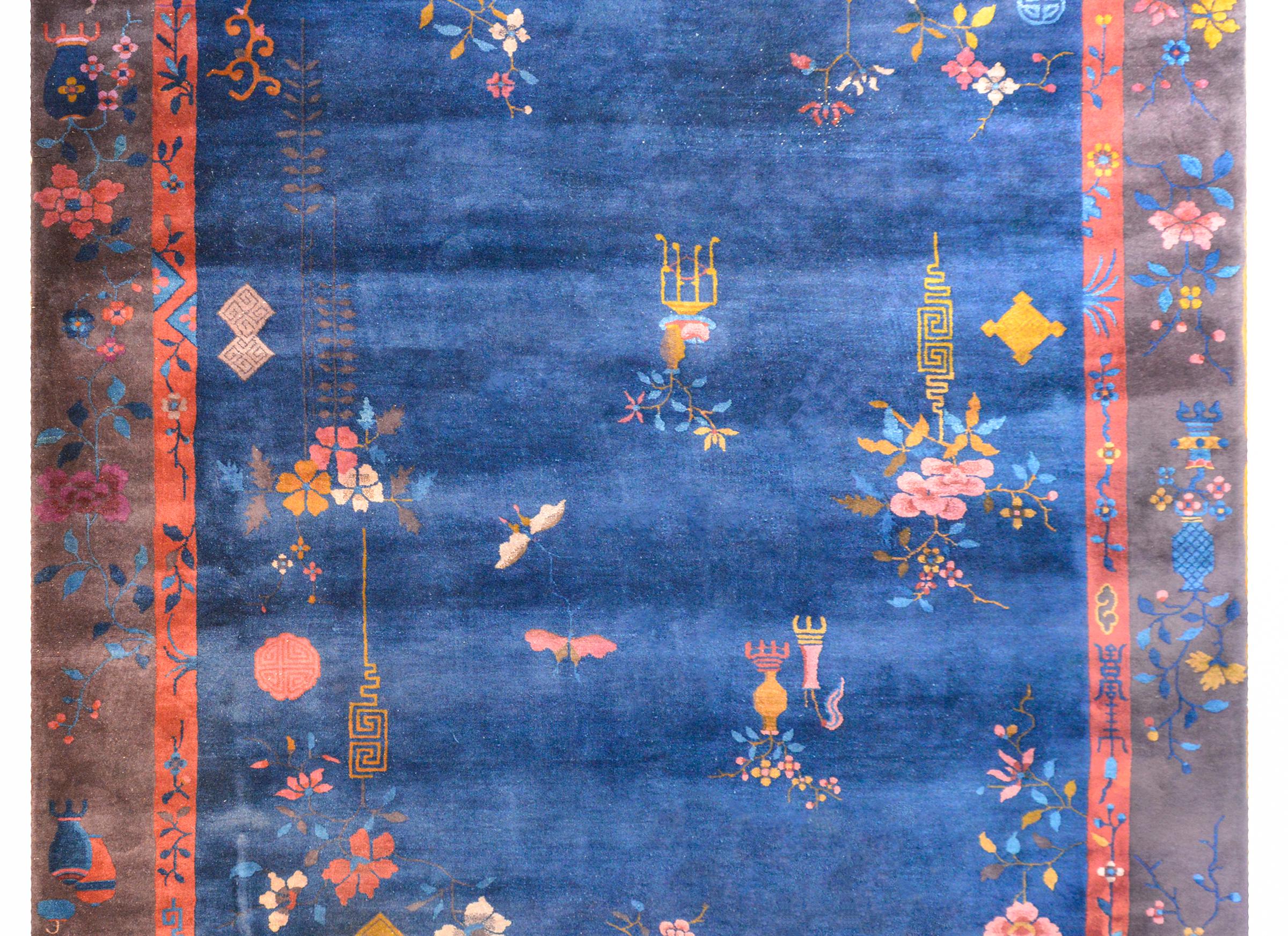 An exquisite Chinese Art Deco rug with an indigo field surrounded by a wide brown outer border with a thin orange inner border all overlaid with myriad auspicious flowering branches and planted pots with butterflies and other auspicious symbols