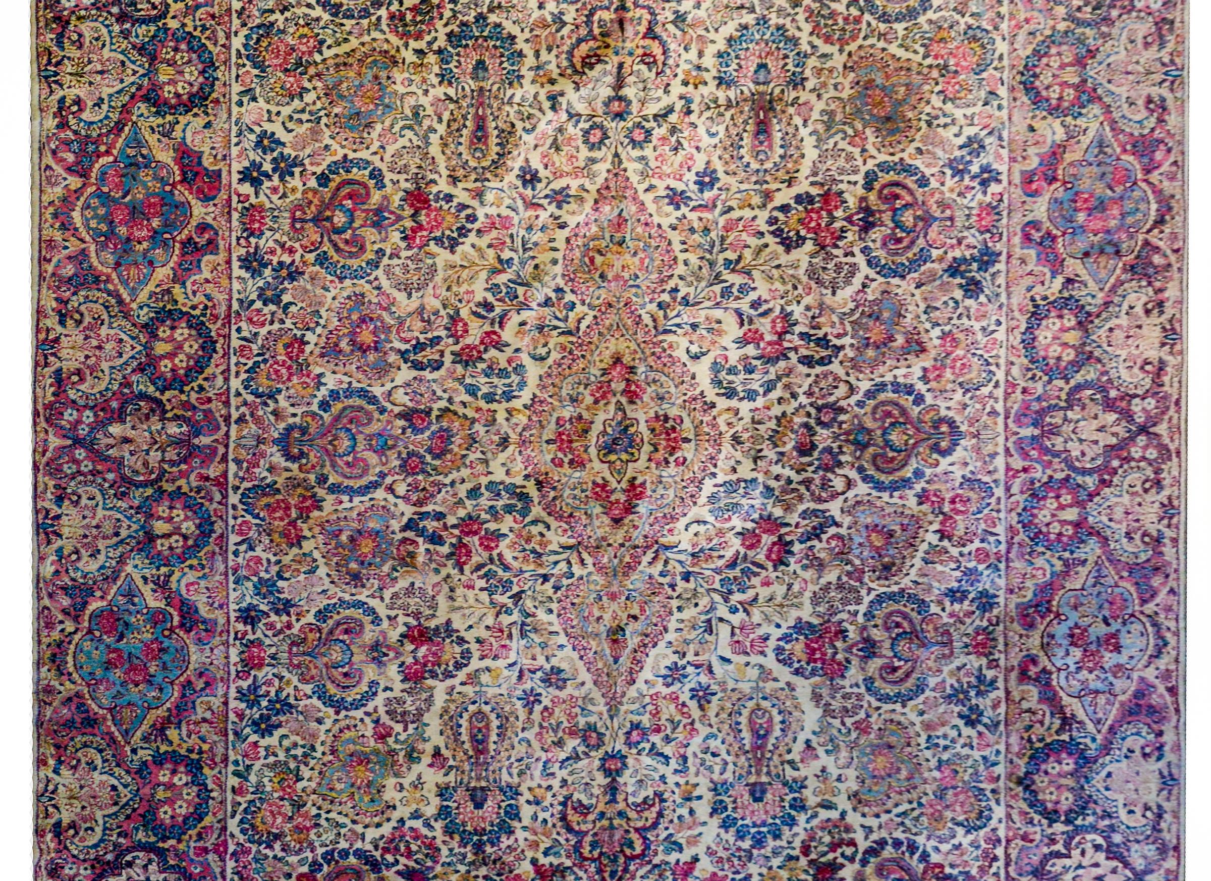 An exquisite early 20th century Persian Lavar Kirman rug with an elaborately woven multicolored design of scrolling vines with myriad flowers woven in light and dark indigo, crimson and rose, and gold vegetable dyed wool, on a cream colored wool