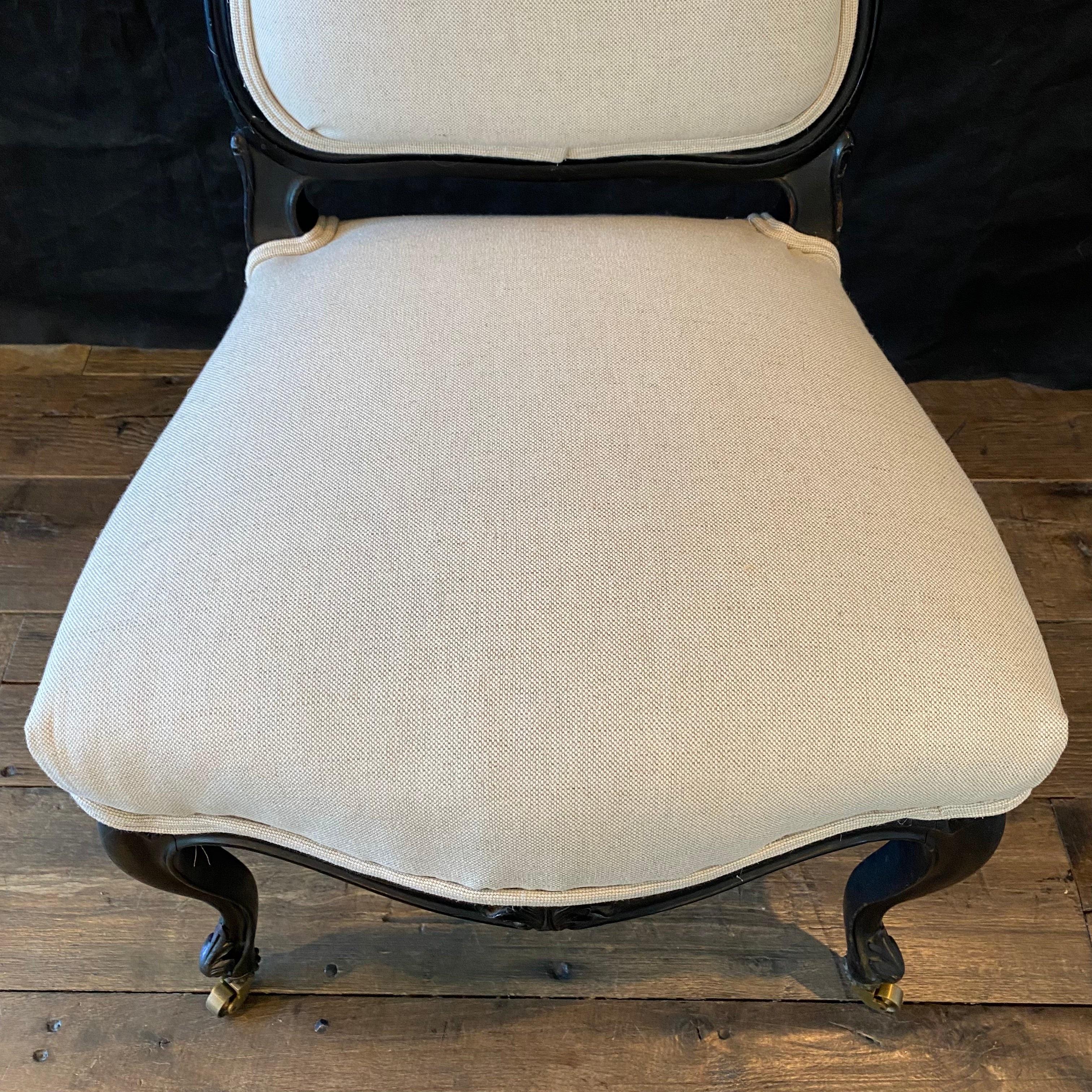 Lovely French Louis XV ebony chair newly reupholstered in a neutral high end British linen cotton blend. There are brass rolling casters on the front, intricate floral carving on the apron and back, and solid wood construction, all supported by