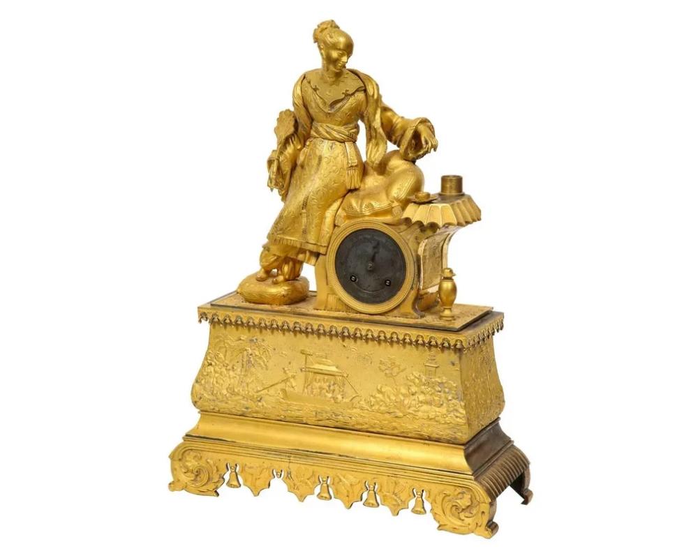 Exquisite French Charles X ormolu bronze chinoiserie figural table clock, early 19th century.

Depicting a Chinese woman wearing jewelry, dressed in her elaborate garments, holding a fan, resting on her saddle throne. The clock case depicting the