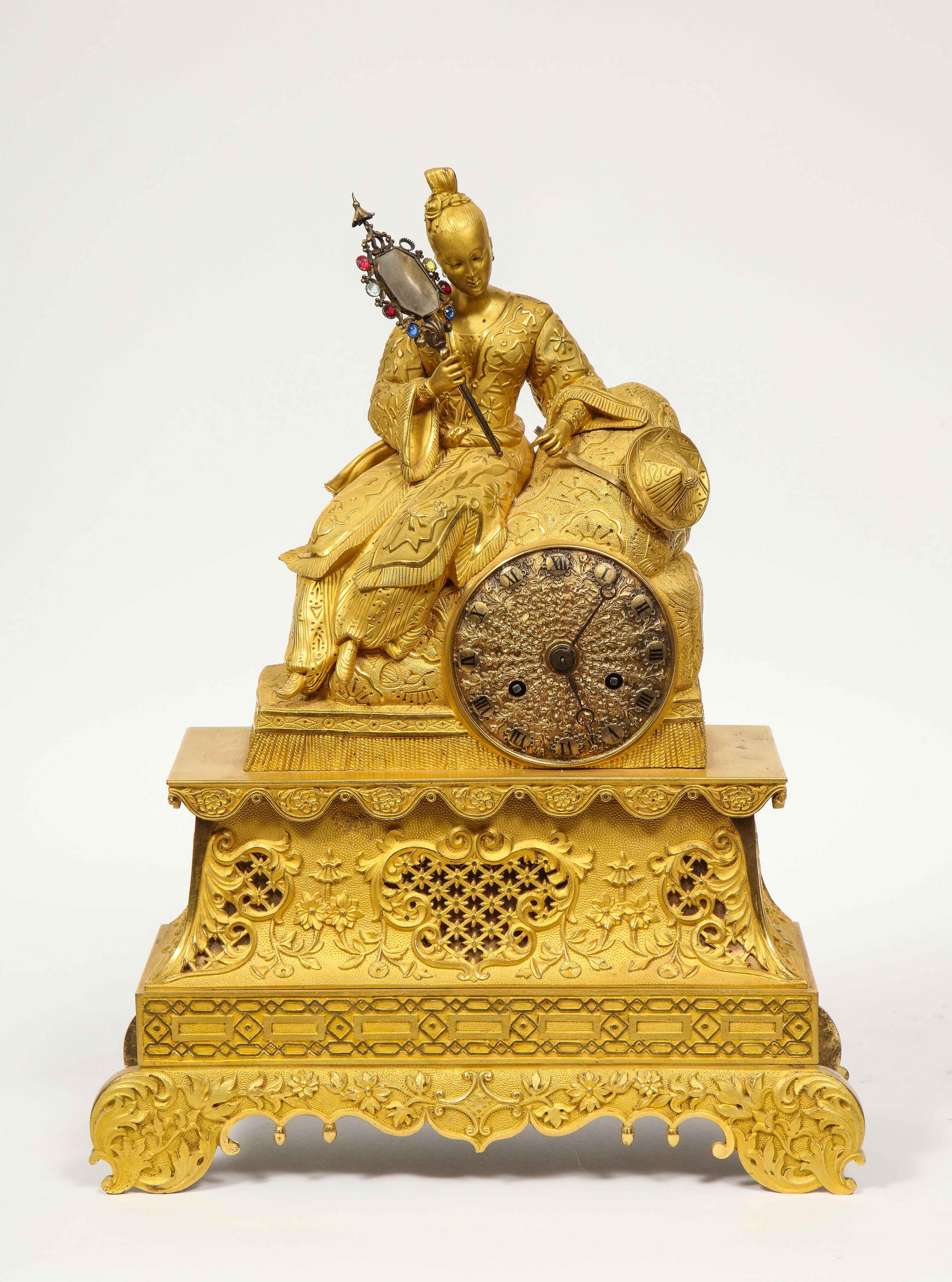 Exquisite French Charles X-Ormolu and jeweled bronze chinoiserie figural table clock, early 19th century.

Depicting a seated Chinese woman holding a jeweled mirror in one hand and her hat in another hand, dressed in her elaborate garments,. The