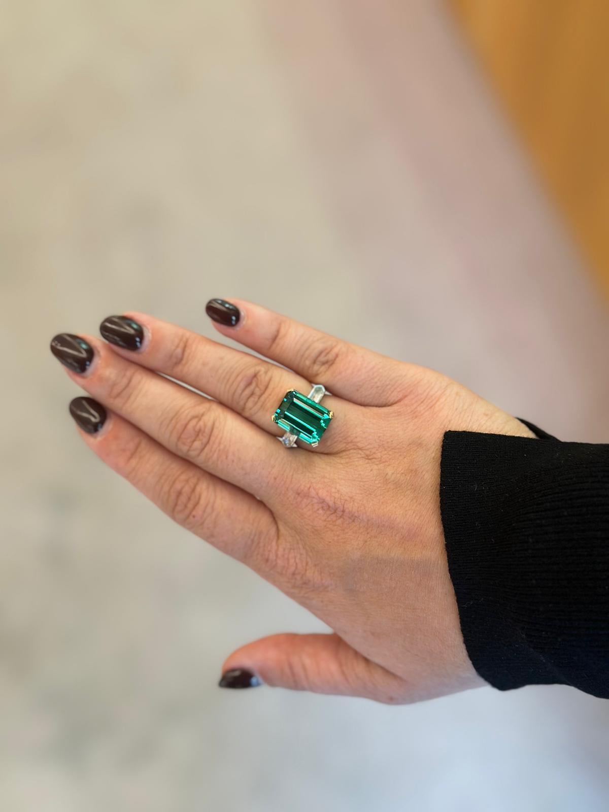 Célébration audacieuse de l'élégance intemporelle et du savoir-faire suisse, cette bague fabriquée à la main est ornée d'une tourmaline verte de 11,62 carats, taillée en émeraude. Flanquée de deux diamants de couleur D taillés en ogive, totalisant