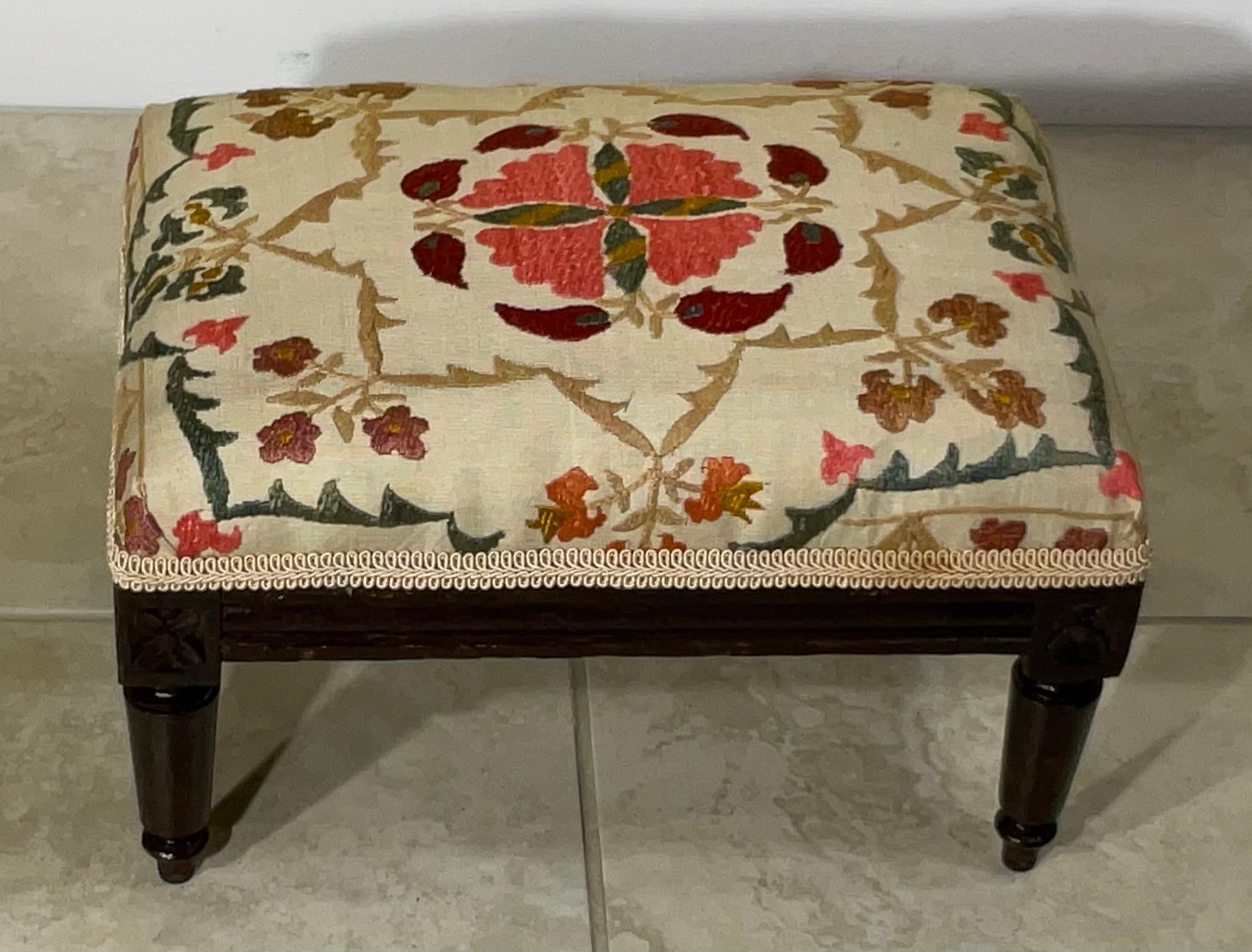 Bringen Sie einen Hauch von Kunstfertigkeit und lebendiger Geschichte in Ihren Wohnbereich mit diesem einzigartigen, mit Suzani-Stickerei gepolsterten Holzschemel. Dies ist nicht einfach nur ein Möbelstück, sondern ein Zeugnis jahrhundertealter