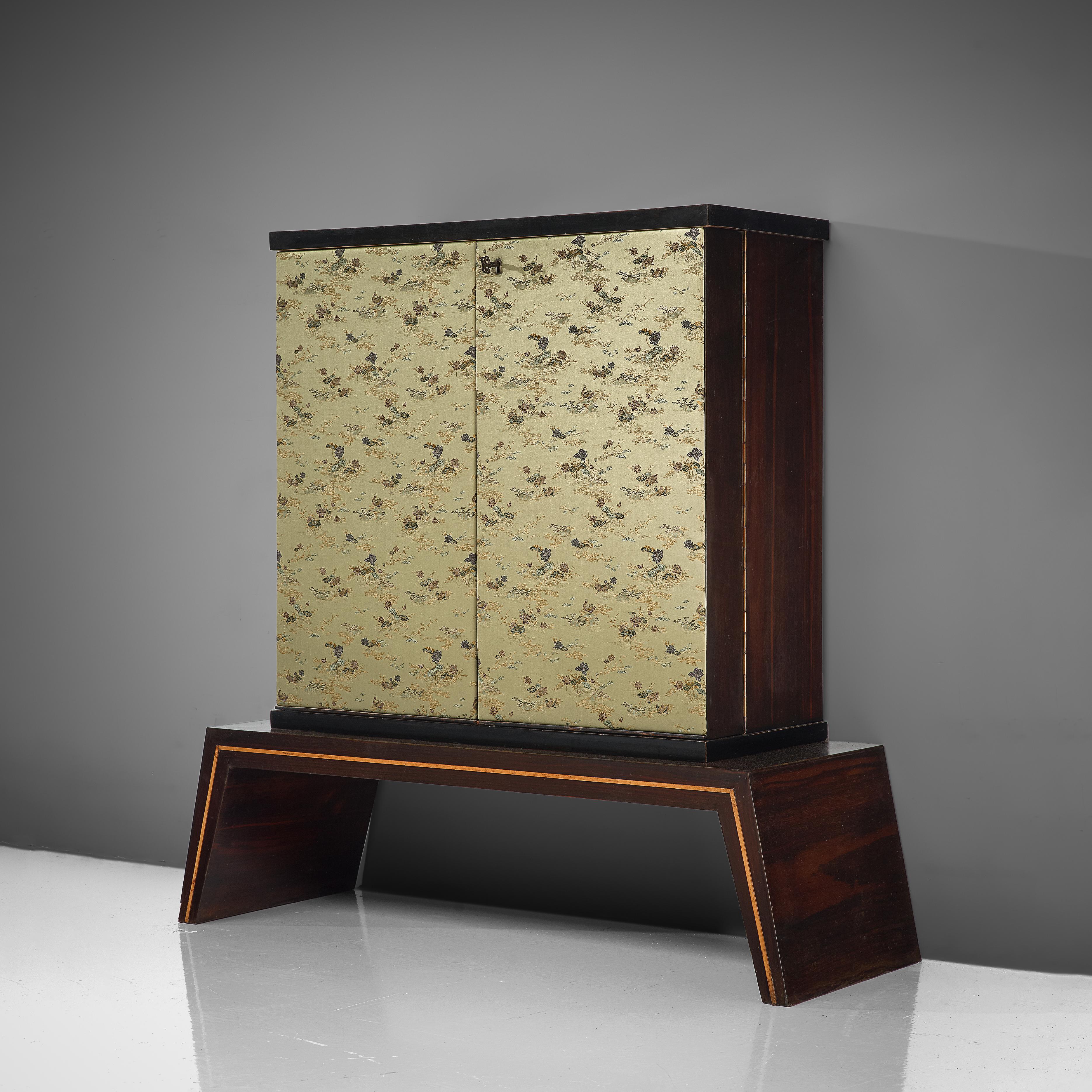 Dry bar cabinet, silk fabric, rosewood, glass, Italy, 1950s

This exquisite dry bar cabinet features a striking contrast between the outside and the design of the inside. Firstly the cabinet stands on a geometric base that consists out of one shape.