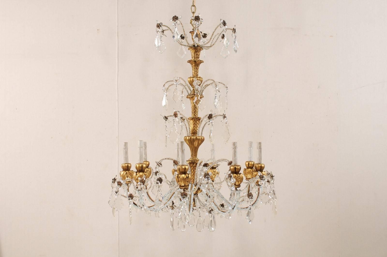 A vintage Italian nine-light crystal and wood chandelier. This Italian chandelier from the mid to late 20th century features a tall gilt, painted and beautifully carved wood central column, with a three-tiered crystal and Italian glass bead