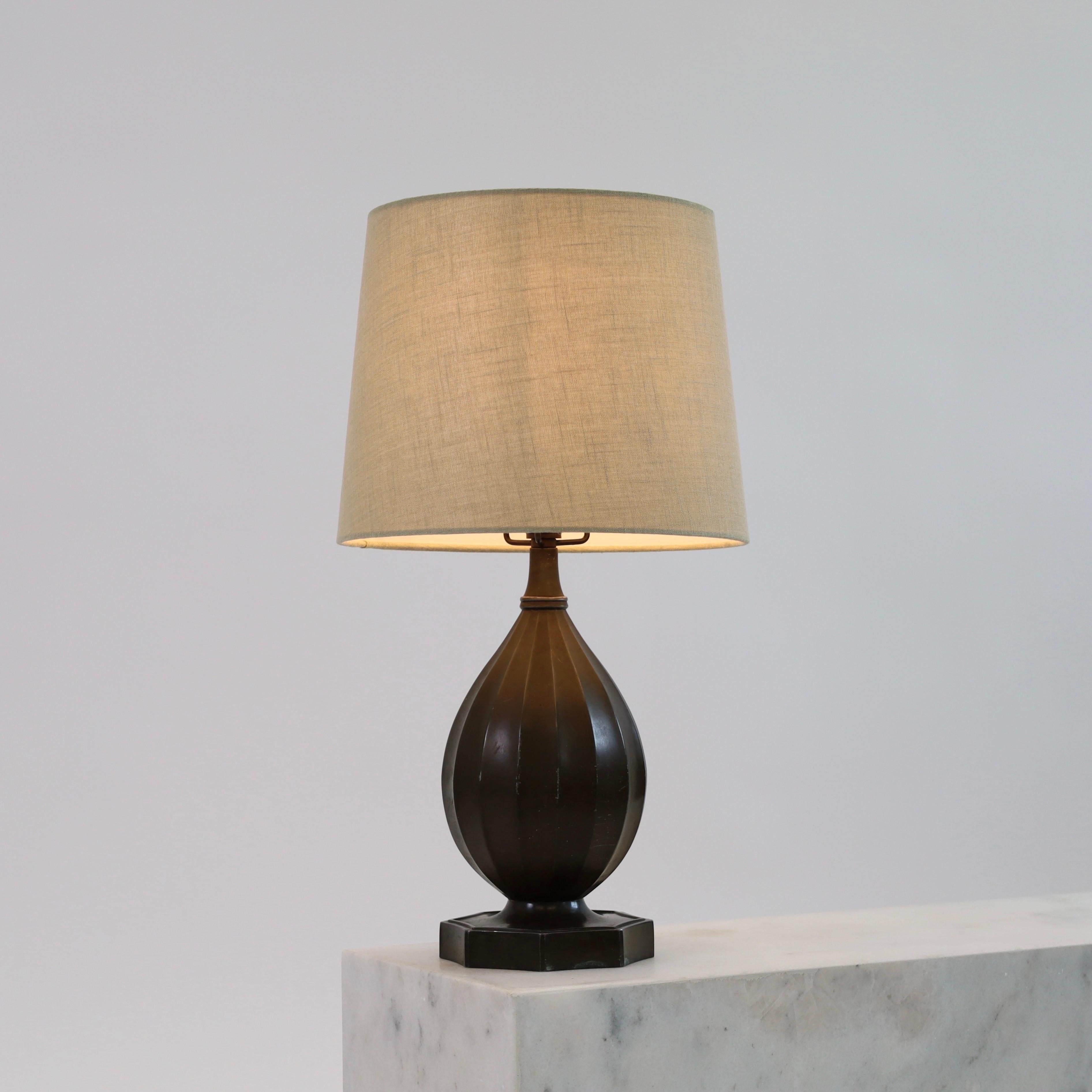 Une lampe de table intemporelle créée par Just Andersen en 1936. Une pièce maîtresse pour une belle maison.  

* Lampe de bureau en métal en forme de bouteille avec des lignes verticales et un abat-jour en tissu beige.
* Designer : Just Andersen
*