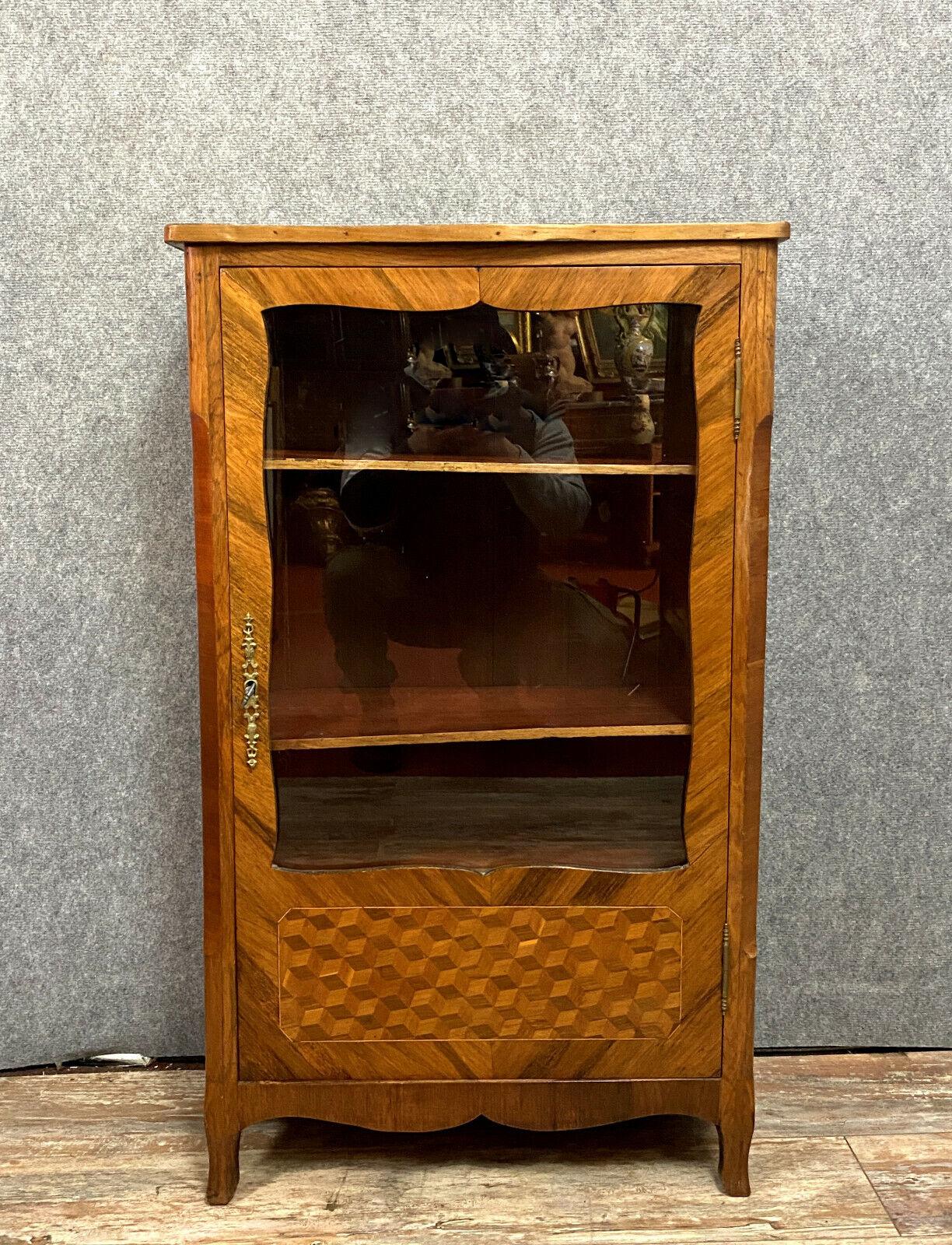 Stunning Louis XV-style bookcase featuring precious wood marquetry.
Front facade opens with a paneled and glazed door for easy access.
Intricate marquetry design showcases cube motifs for added elegance.
Gracefully stands on curved feet, flanked by