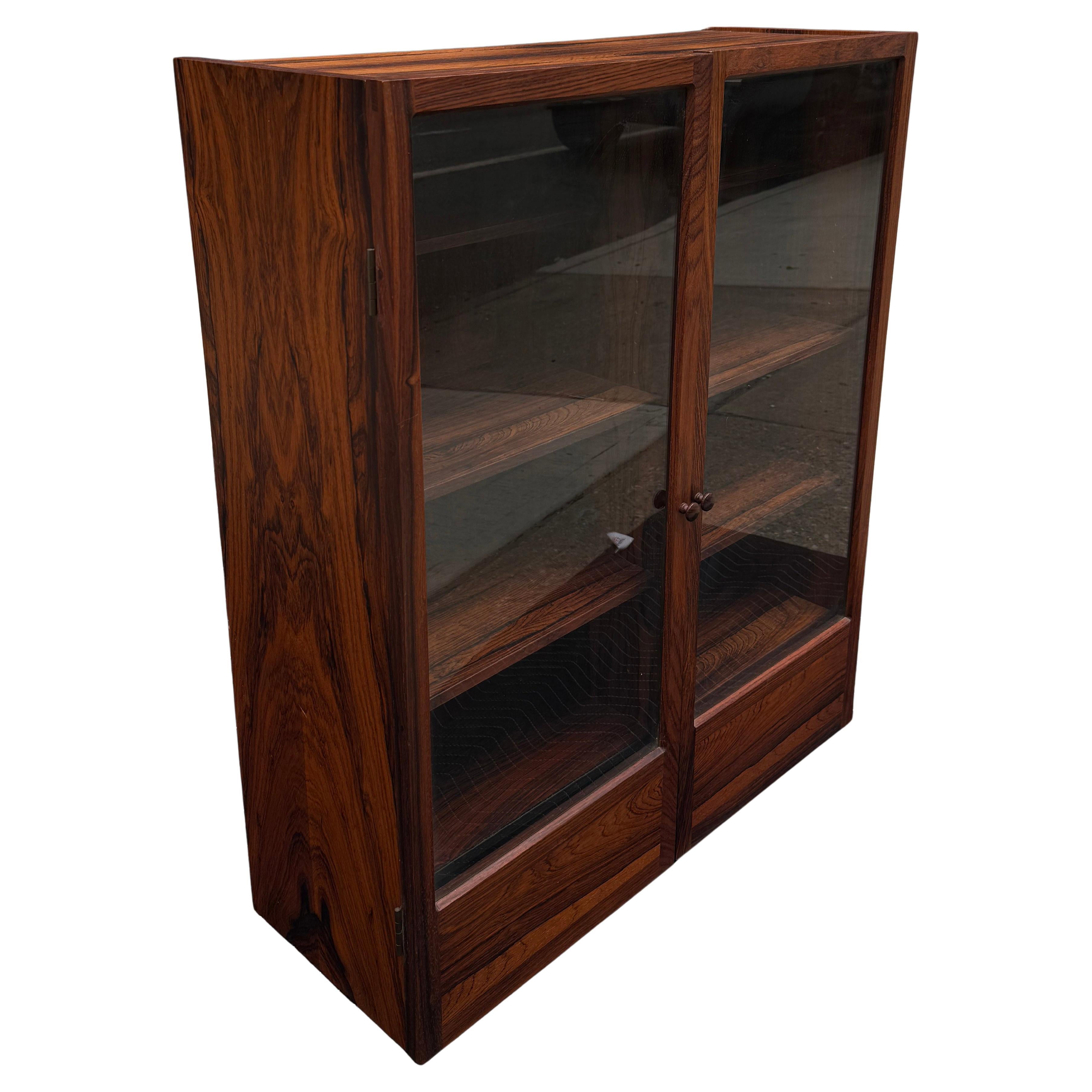 Eleva il tuo spazio con questa raffinata vetrina danese moderna a parete. Realizzato in un'elegante forma rettangolare, presenta due ante vetrate che si aprono per rivelare un interno con diversi ripiani regolabili, perfetti per esporre oggetti da