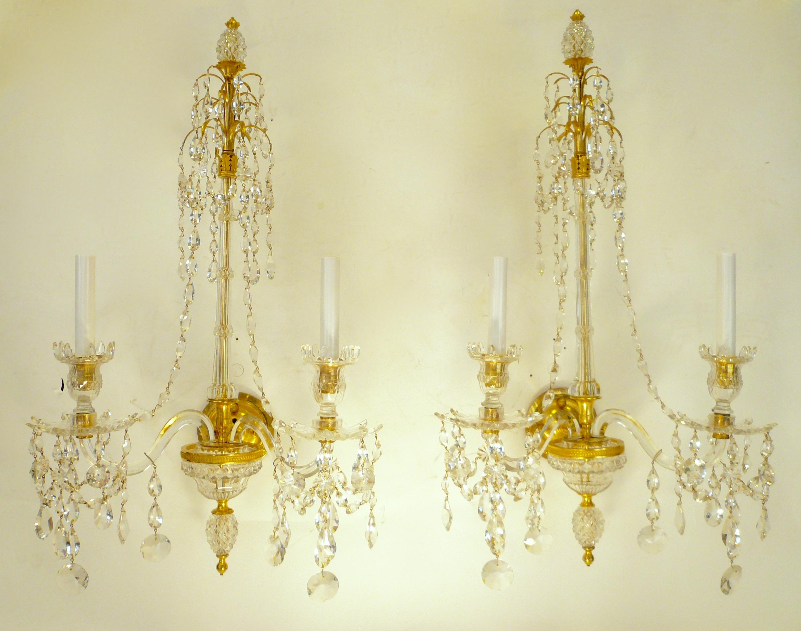 This fabulous pair of ormolu mounted cut crystal twin arm sconces are attributed to William Parker.
In the Adam taste these sconces feature Neo-Classical motifs, including hand chased gilt bronze acanthus leaves, scrollwork, and faceted crystal