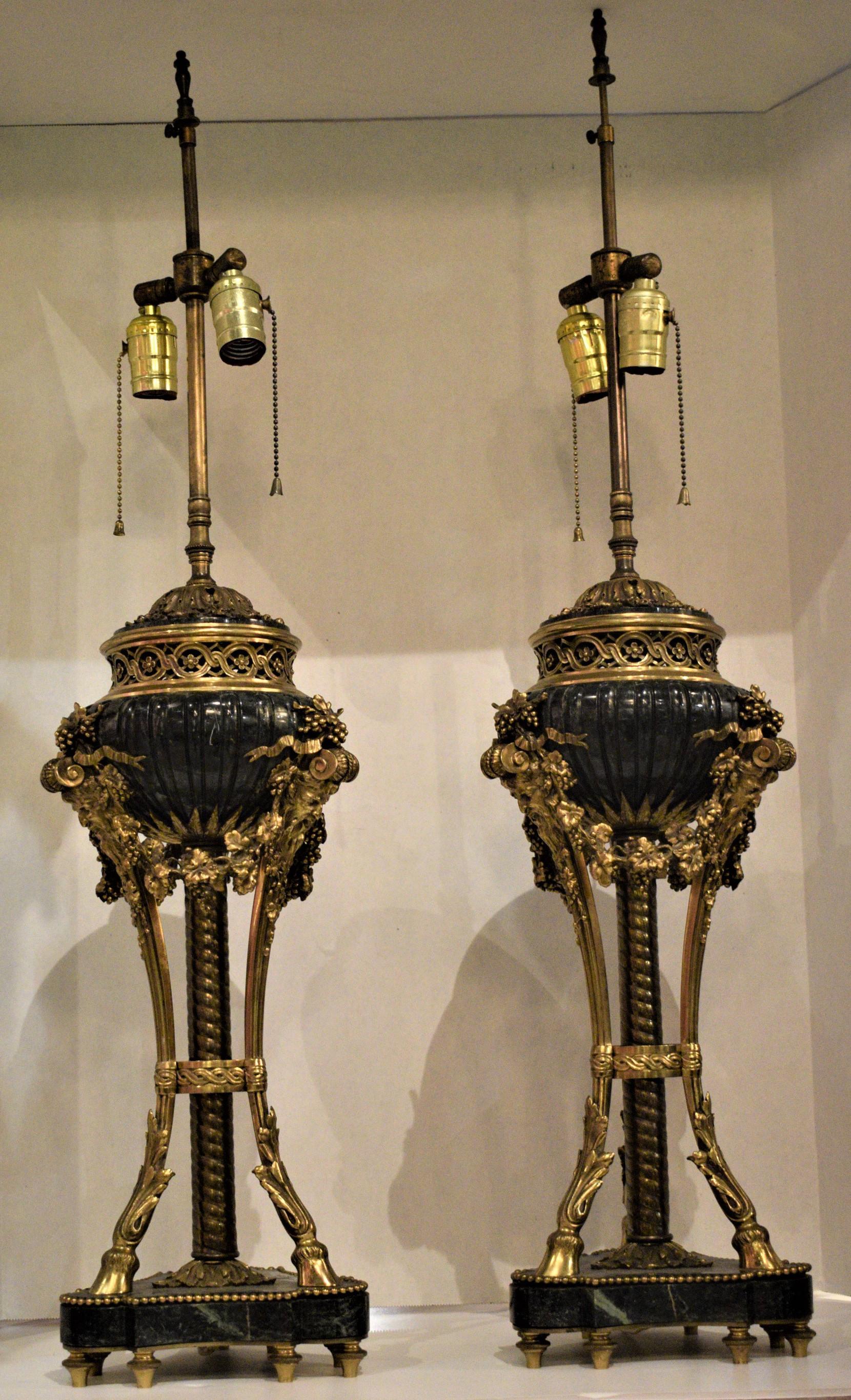 Exquisite pair of gilt bronze and marble lamps depicting Bacchus masks, garlands with grapes and leaves supported by three feet ending on hooves, on the bottom a marble plinth raised on turned toupie feet. On top a pierced gallery. These were