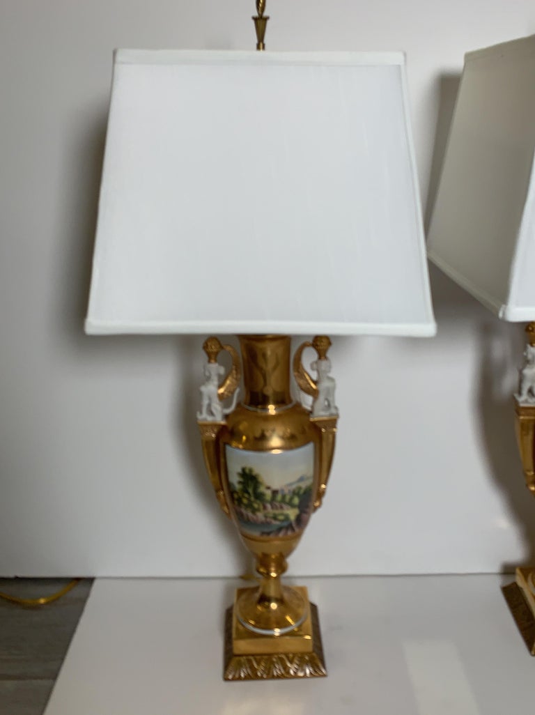 A pair of late 19th century neoclassical urns now as lamps. The beautifully decorated Paris porcelain with bucolic scenes on the main body with female sphinx porcelain bisque handles. The exceptional two tone gilt on the urns in very good well cared