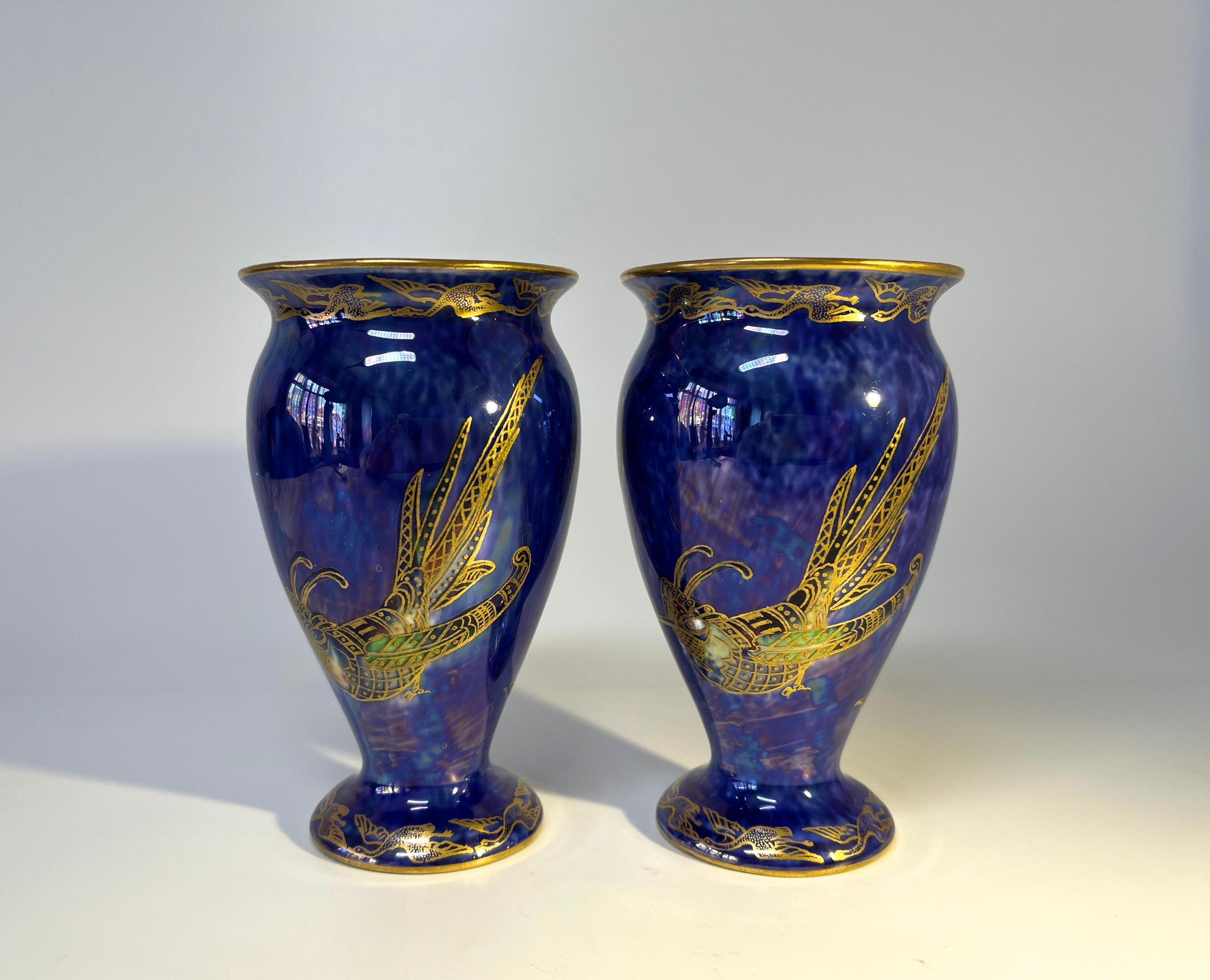 Paire exquise de vases balustres lustrés ordinaires de Wedgwood par Daisy Makeig-Jones. Circa 1915.
Dominée par de spectaculaires oiseaux exotiques dorés à crête sur un fond bleu royal chiné d'une incroyable richesse.
Des oies volantes dorées