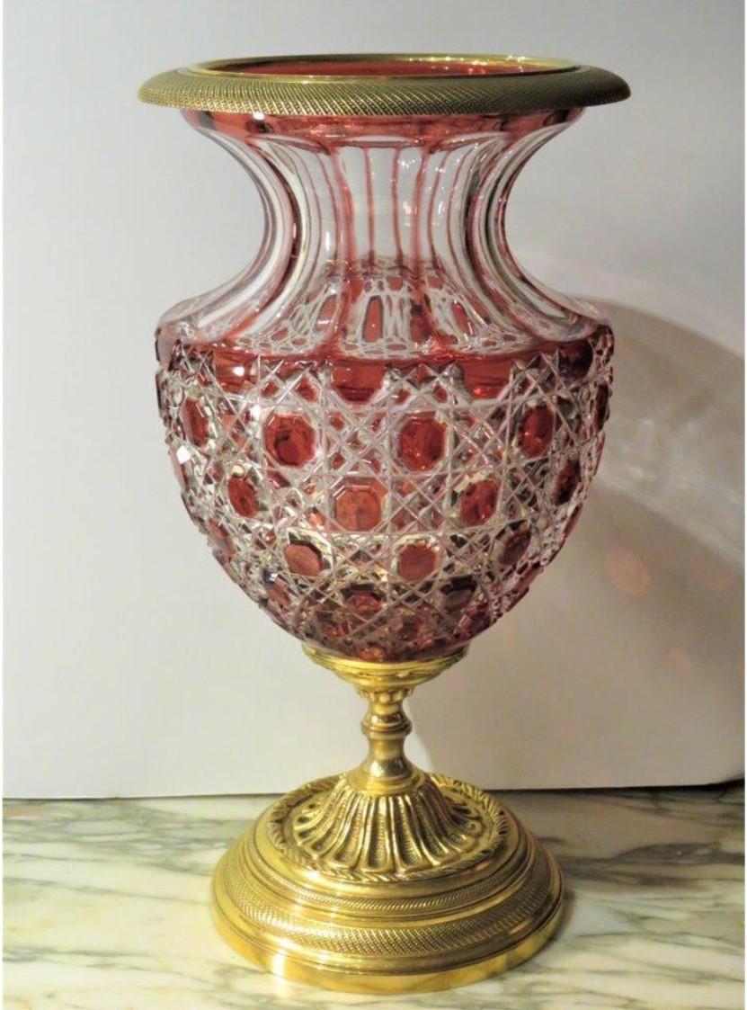 El siguiente artículo que ofrecemos es una magnífica urna florero de bronce con centro de mesa de cristal rojo tallado a mano de estilo Imperio francés. Maravillosamente realizada con pan de oro fino de 24 quilates y bronce dorado, con intrincados