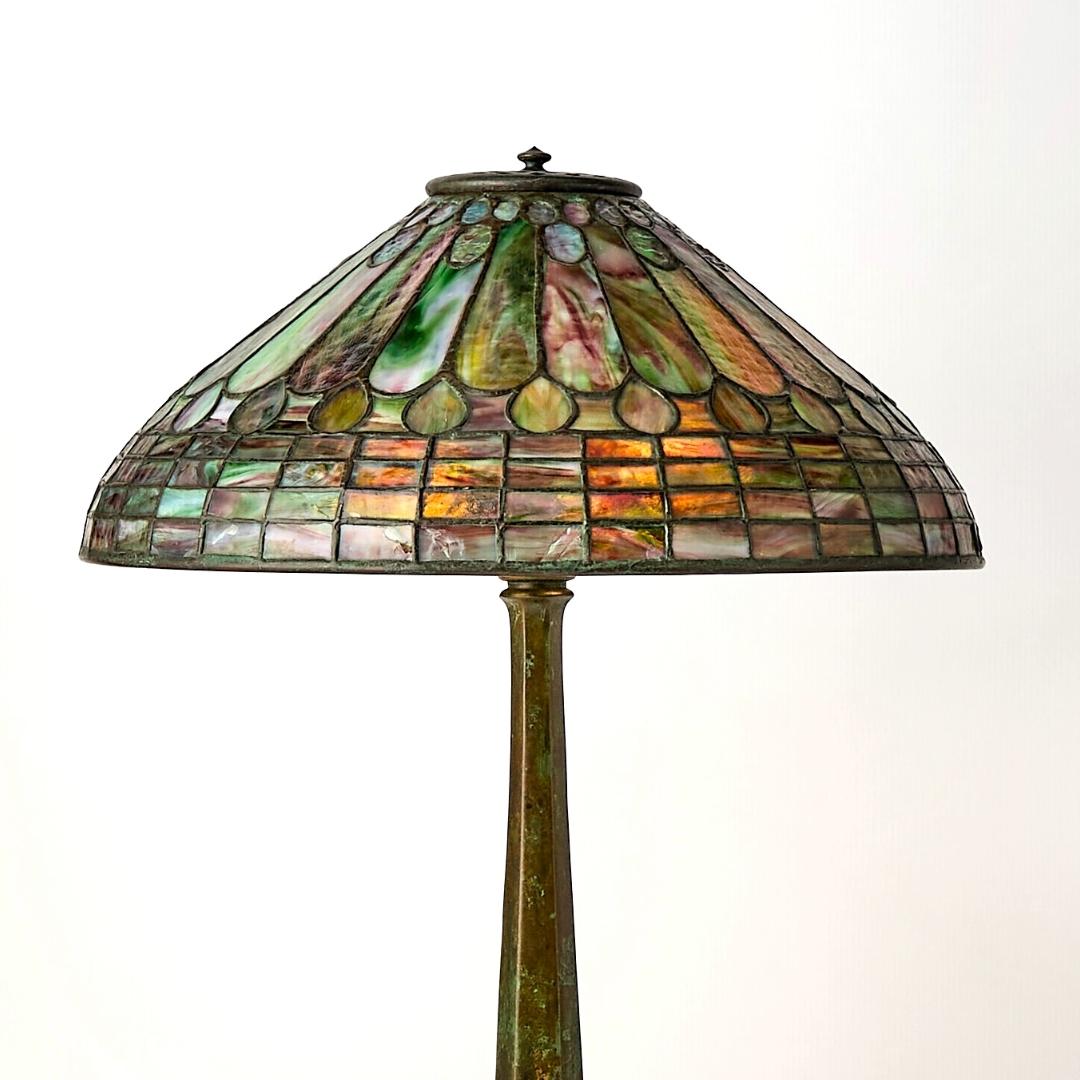 Cette superbe lampe de table des studios Tiffany, datant d'environ 1915, représente l'apogée de l'art décoratif américain du début du XXe siècle. Avec son abat-jour conique raffiné en verre au plomb, magistralement composé de motifs de plumes