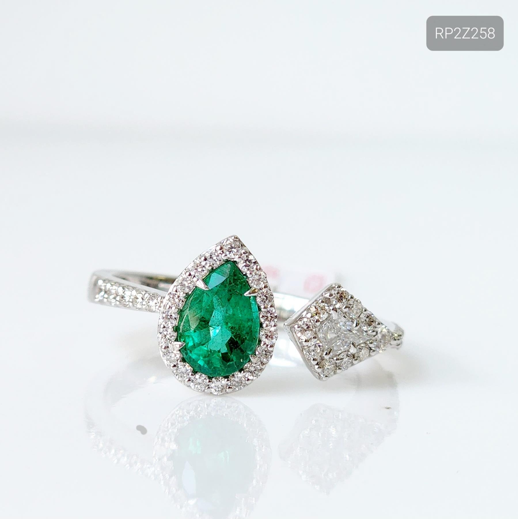 Introducing our exquisite Toi et Moi Emerald and Diamond Ring. This stunning piece showcases a 0.65 carat pear-shaped green emerald as the centerpiece, elegantly surrounded by a halo of glistening 0.31 carat white melee diamonds. The addition of