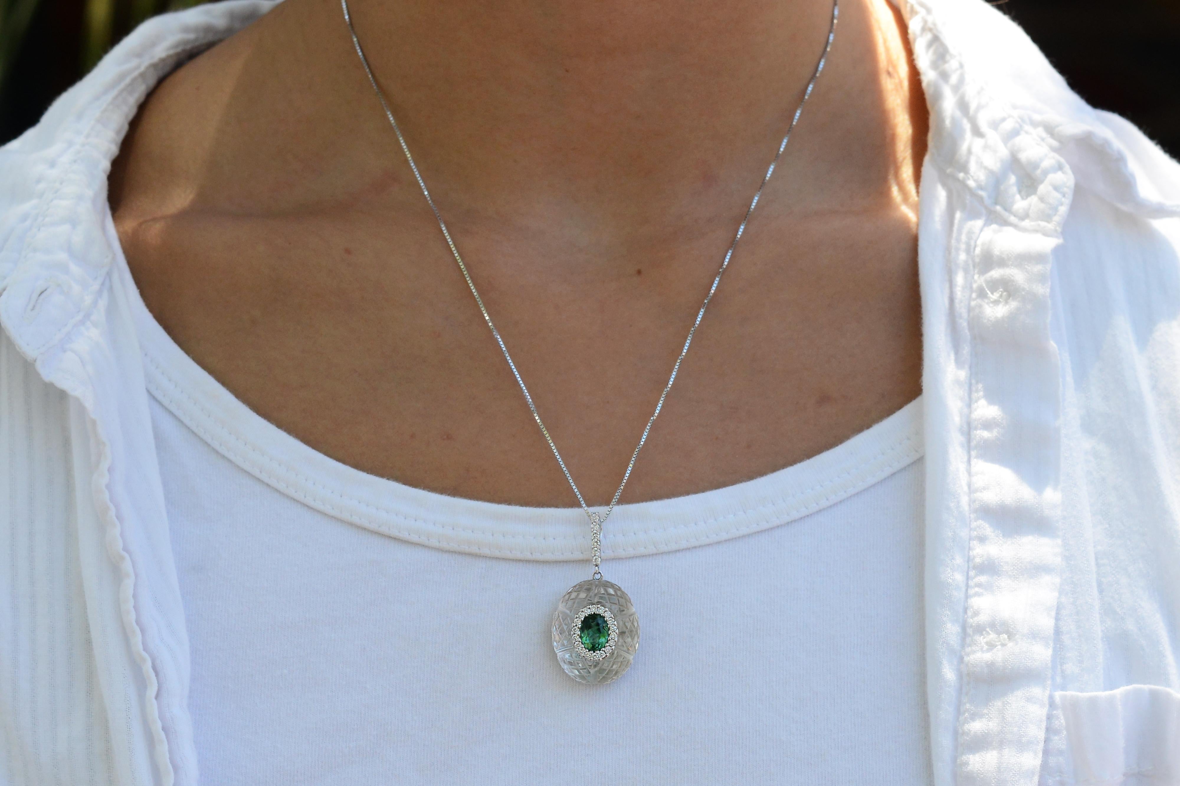 A deluxe pendant offering a captivating blend of classic elegance and modern appeal, reminiscent of the Art Deco era. Crafted with a unique carved rock crystal quartz orb and an electric blue green glowing tourmaline, it is an exquisite and