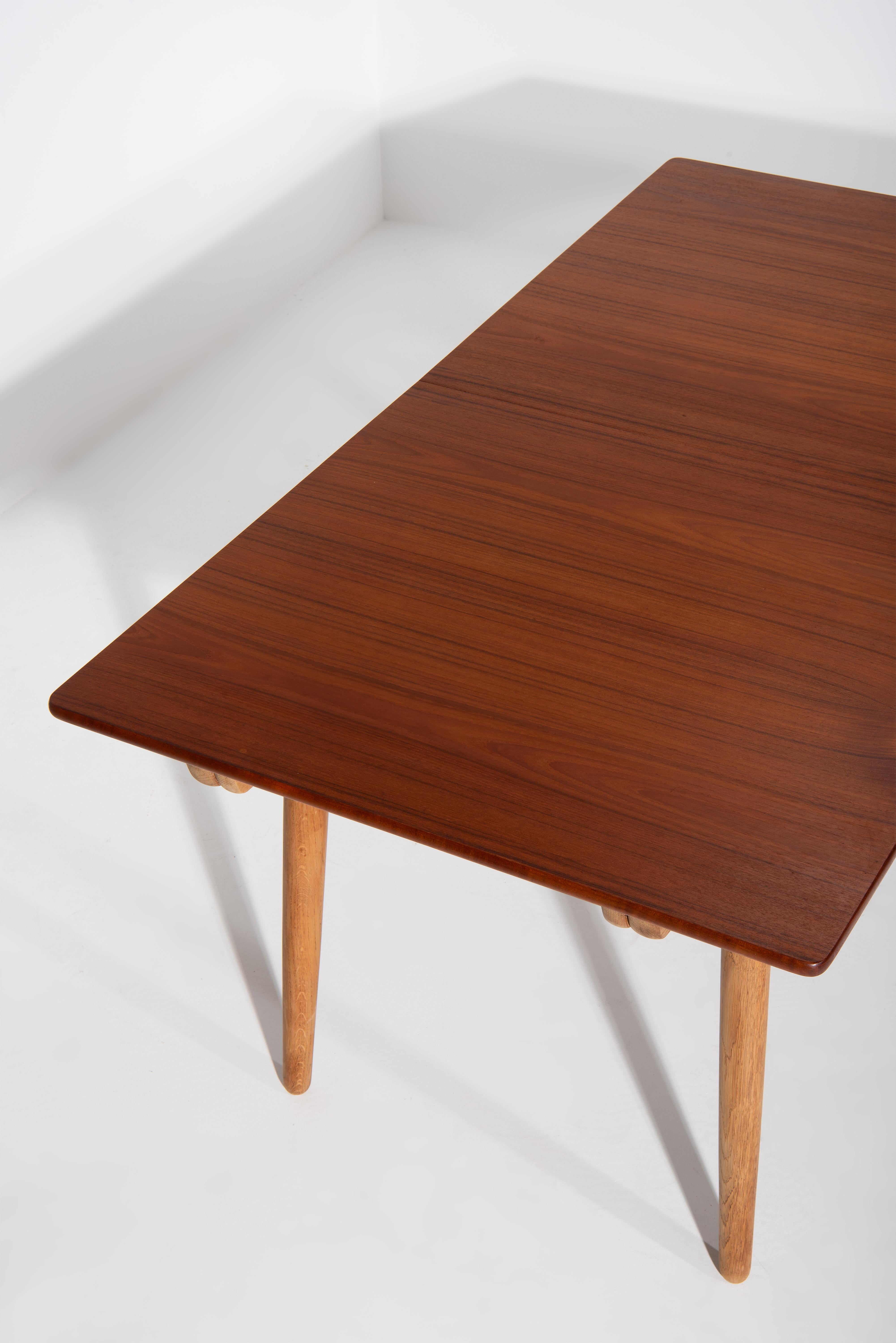 An extendable dining table AT-310 designed by Hans J. Wegner in 1955 for Andreas Tuck in Denmark. The top is made in teak veneer and the base in solid oak. Included are 2 extension leaves that can be stored underneath the table top. Once the two