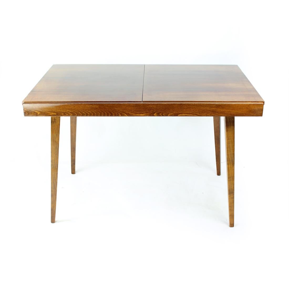 Beautiful extendable dining table produced by Tatra company in Czechoslovakia in 1960s. The table stands on four legs and has beautiful, elegant designed shape. The top board in rectangular with dark, beautiful veneer finished in hugh sheen lack