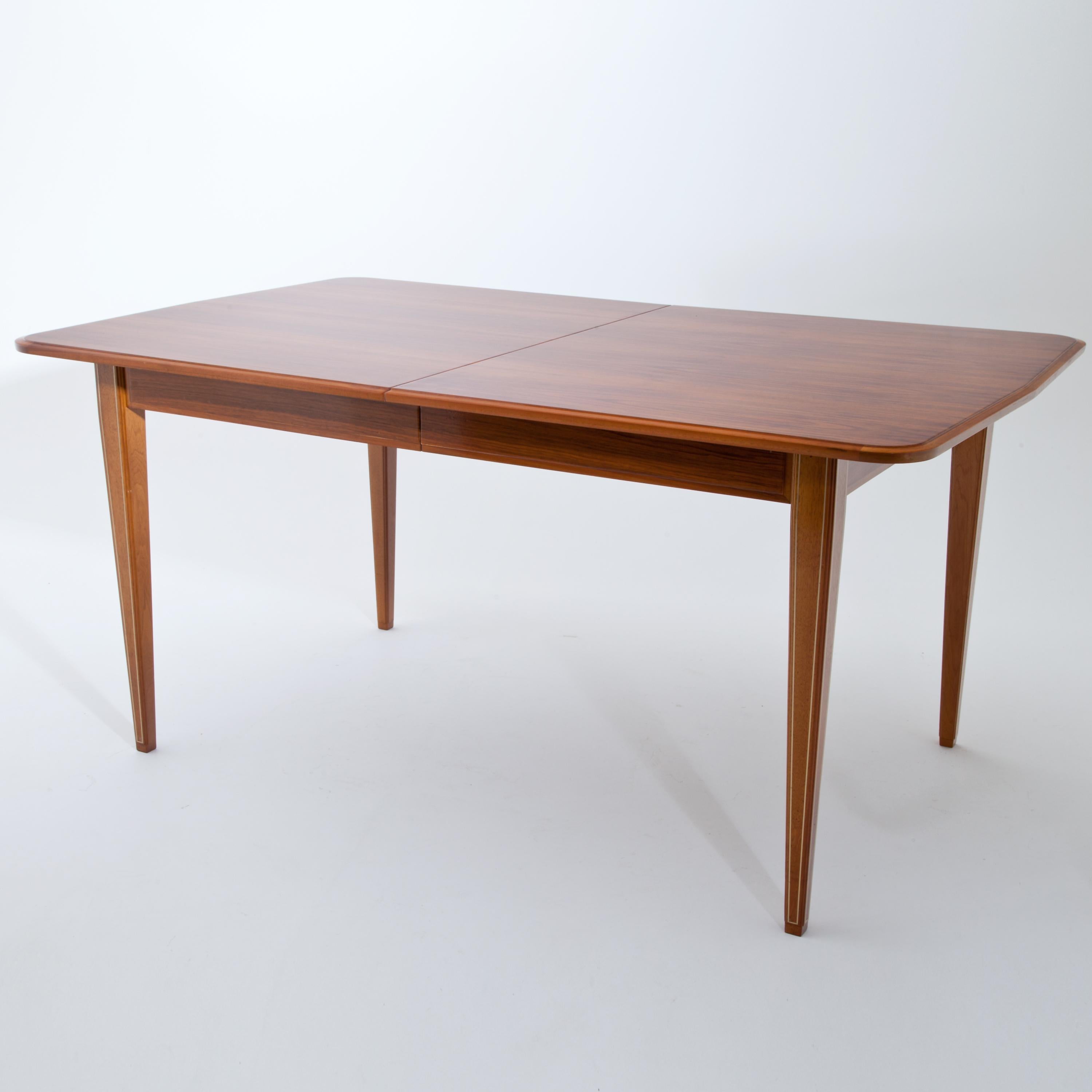Rectangular extendable dining table with square pointed legs and straight smooth frames. The tabletop is profiled at the edges and tapers slightly at the narrow sides. The legs are inlaid with brass threads. Very good restored condition. The maximum