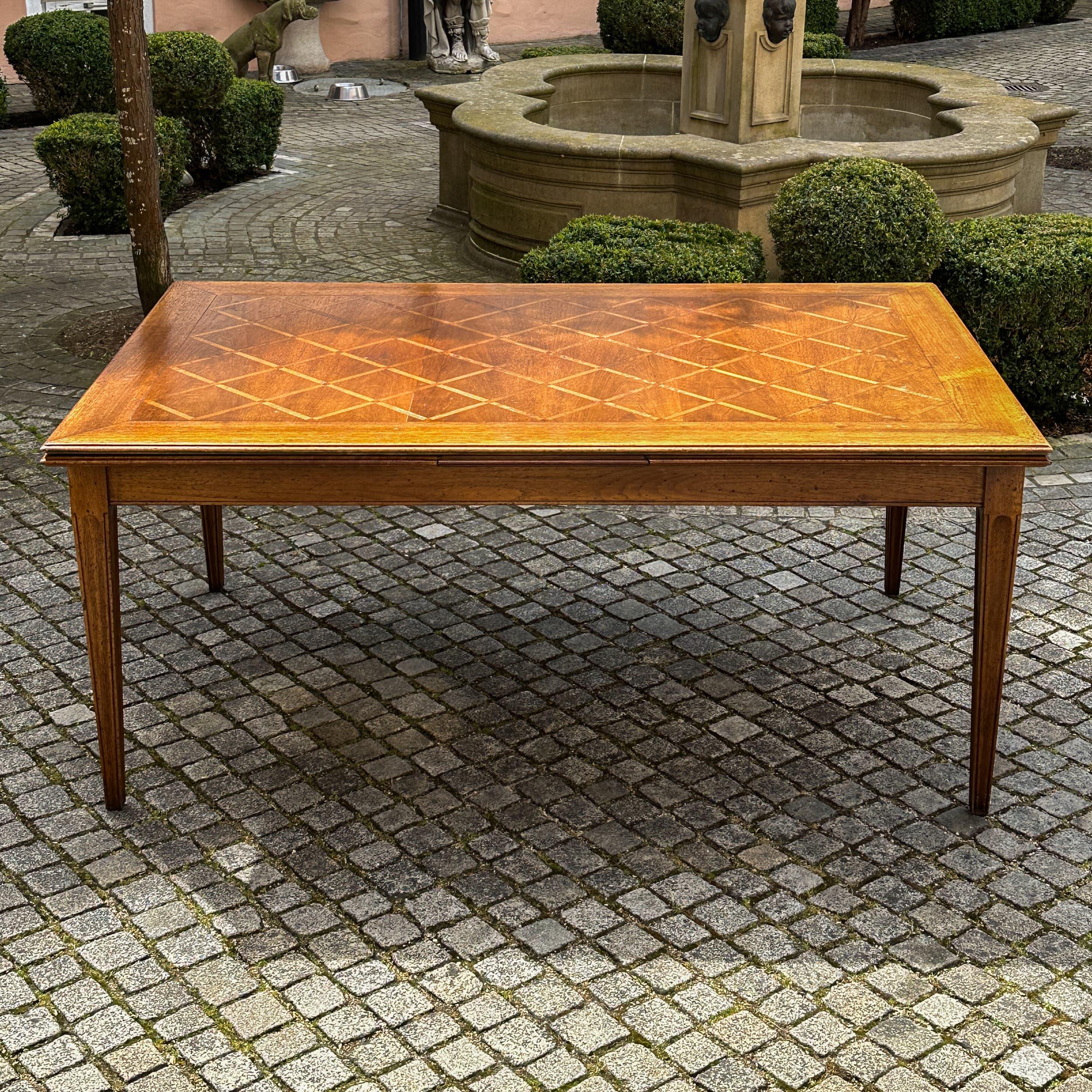Grande table de salle à manger extensible en chêne massif, datant du début du 20e siècle. Le plateau de table présente un motif de parquet en losange et repose sur des pieds fuselés avec des cannelures verticales de style moderne. Deux rallonges