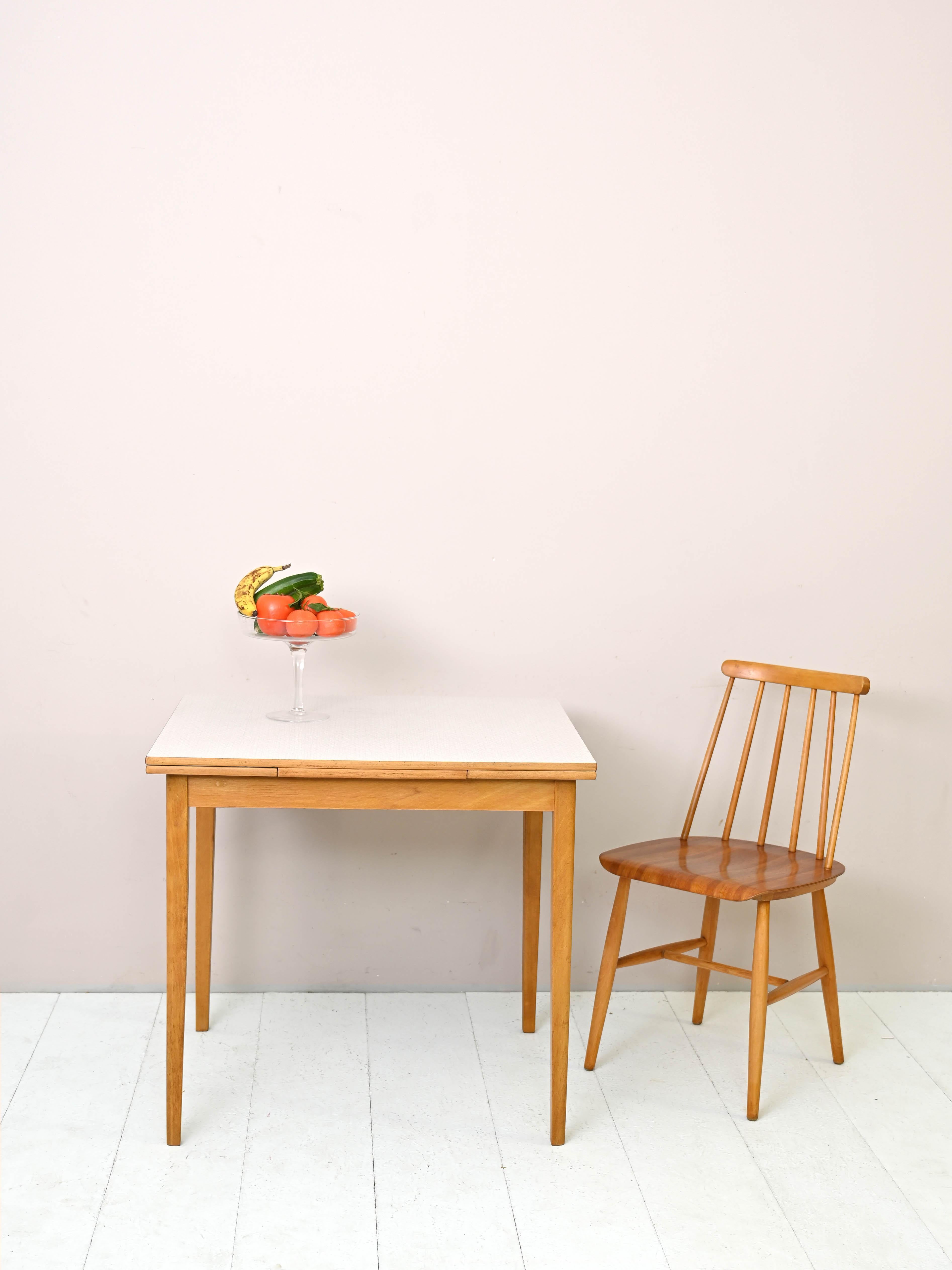 Vintage 1960s wood and formica table.
 
A piece of furniture with classic mid-century lines. The profile and long tapered legs are made of light oak, giving it a modern and original look.
There are two retractable side extensions that allow the
