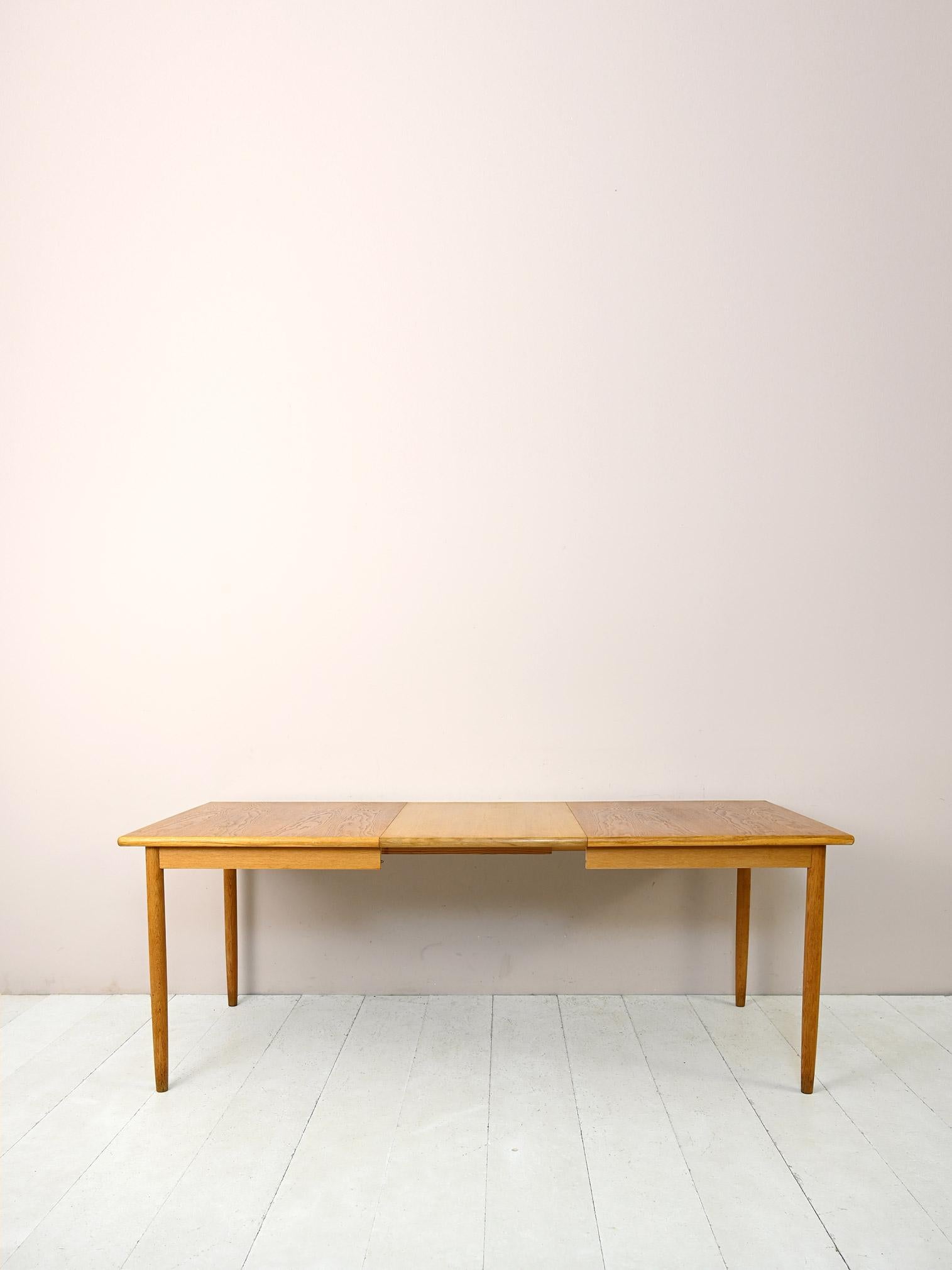 Table vintage des années 1960 avec rallonges centrales.

Ce meuble antique moderne aux formes essentielles et minimalistes se compose d'un grand plateau rectangulaire aux angles arrondis et de longs pieds coniques.
Grâce à la possibilité d'être