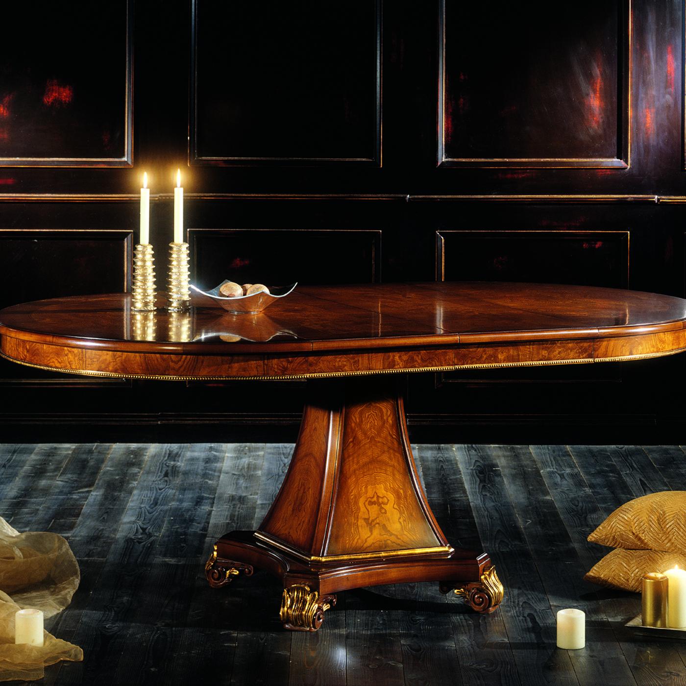 This extendable table boasts walnut veneer and ash burl. The pedestal base has a faceted sloped silhouette raised on a platform with four ornate feet. The round top measures 120 cm and features a linear inlay in bois de rose and a semi-gloss finish