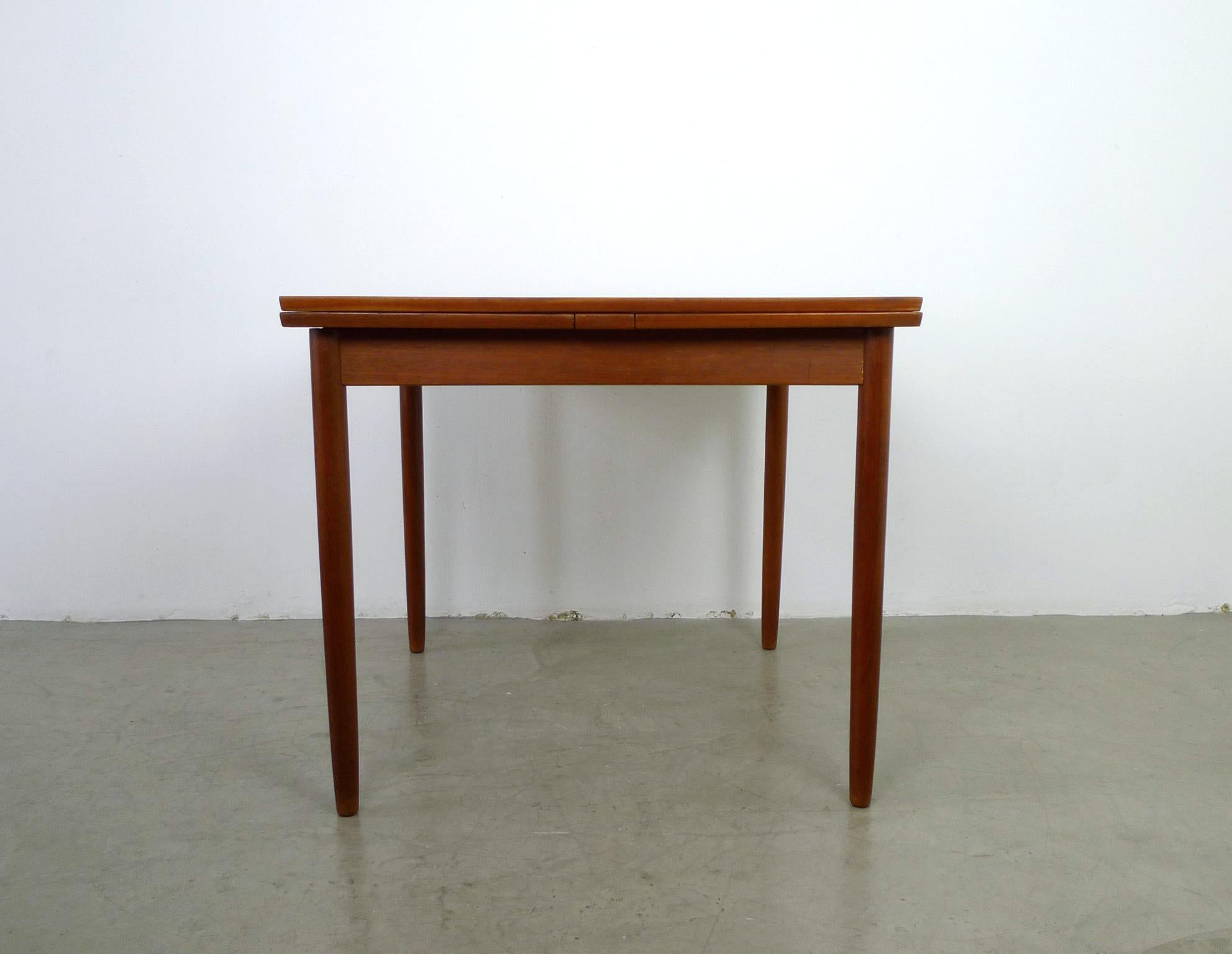 This piece is a square teak dining table with two 38 cm extension plates that extend the table to a total length of 161 cm. The table dimensions without extension plates are given below. The dining table was made in Denmark in the 1960s and it is in