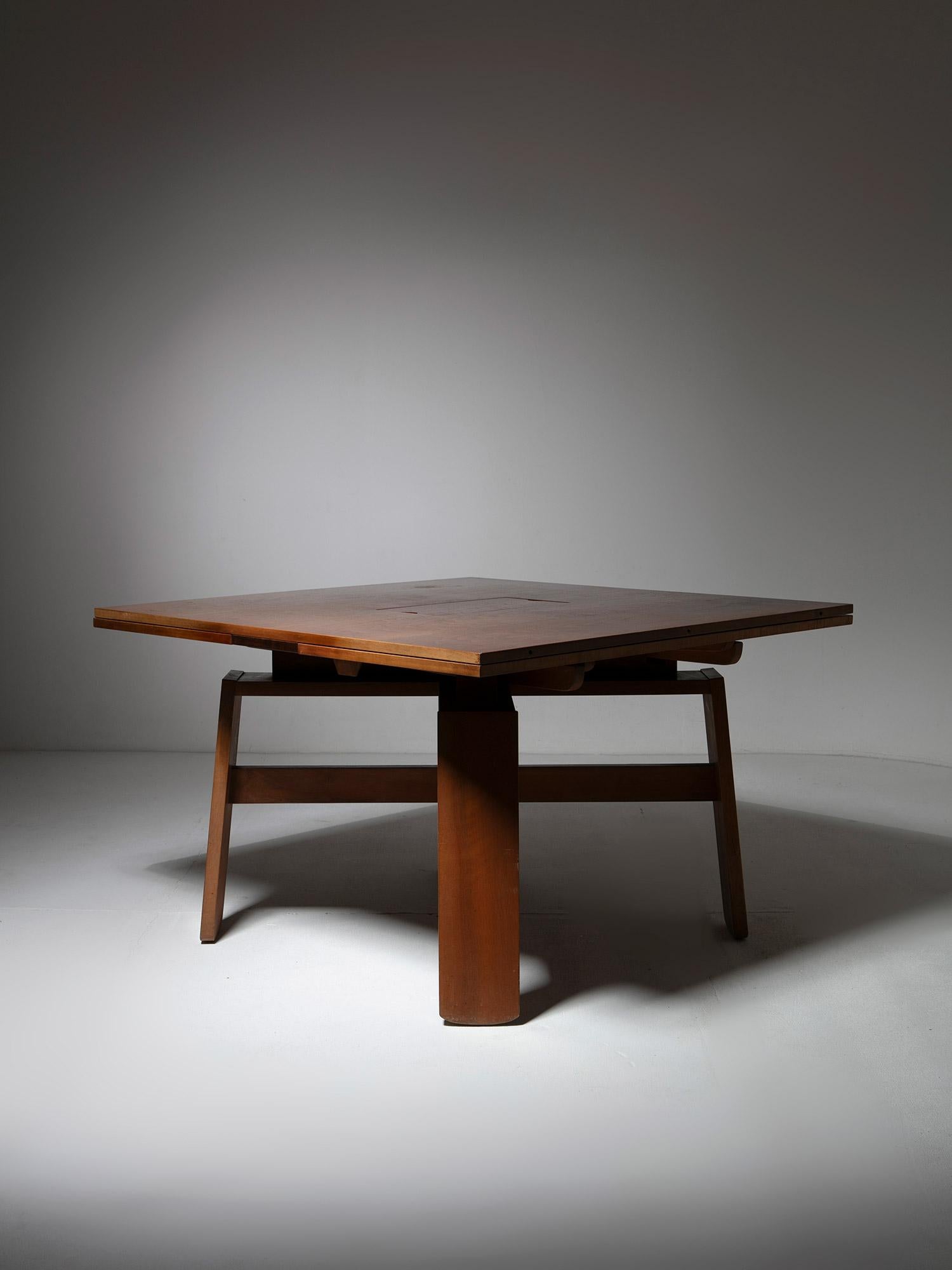 Extendible dining table model 612.1 by Sivlio Coppola for Bernini.
Sculptural walnut frame supporting a squared top with hidden wings and two white ceramic trays.
Width goes from cms 115 to 210 