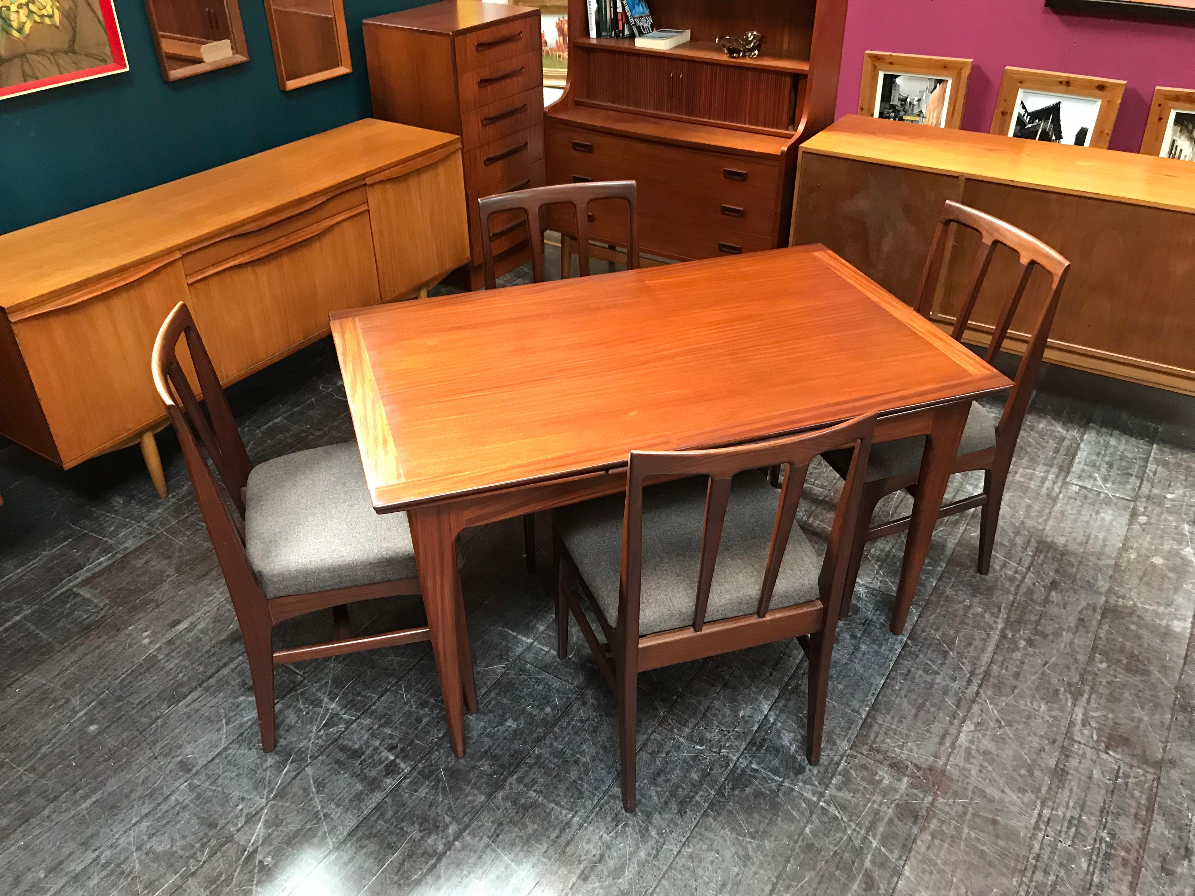 An extending dining table and 4 chairs made from afrormosia wood and designed by John Herbert for A. Younger Ltd. This elegant, vintage mid-century dining set is of very high quality design and construction, with beautifully shaped legs. The chairs