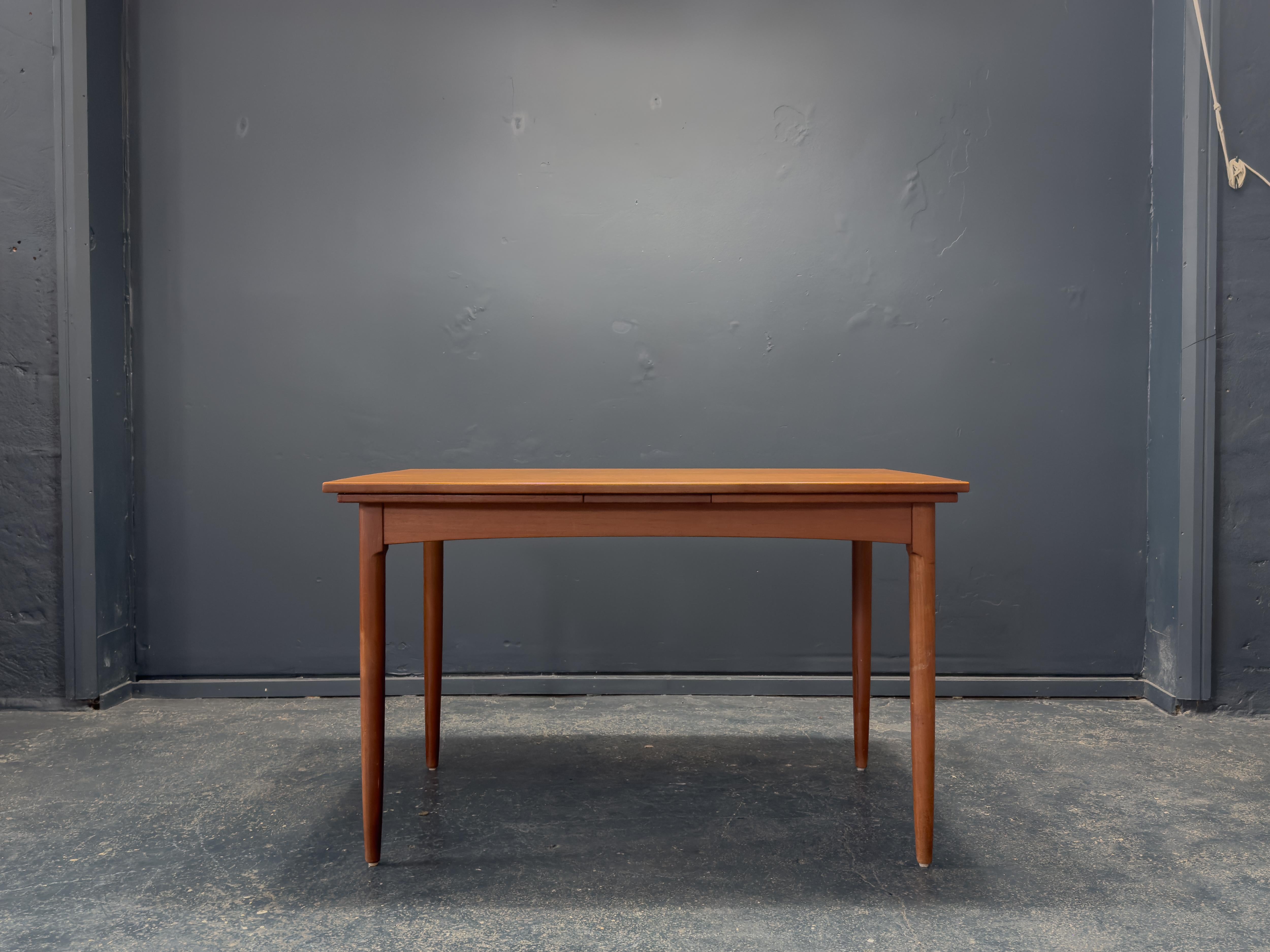 Cette élégante table de salle à manger extensible en teck présente les caractéristiques de l'artisanat nordique du milieu du siècle avec ses lignes épurées, son design fonctionnel et sa finition chaude en teck richement grainé. Le plateau