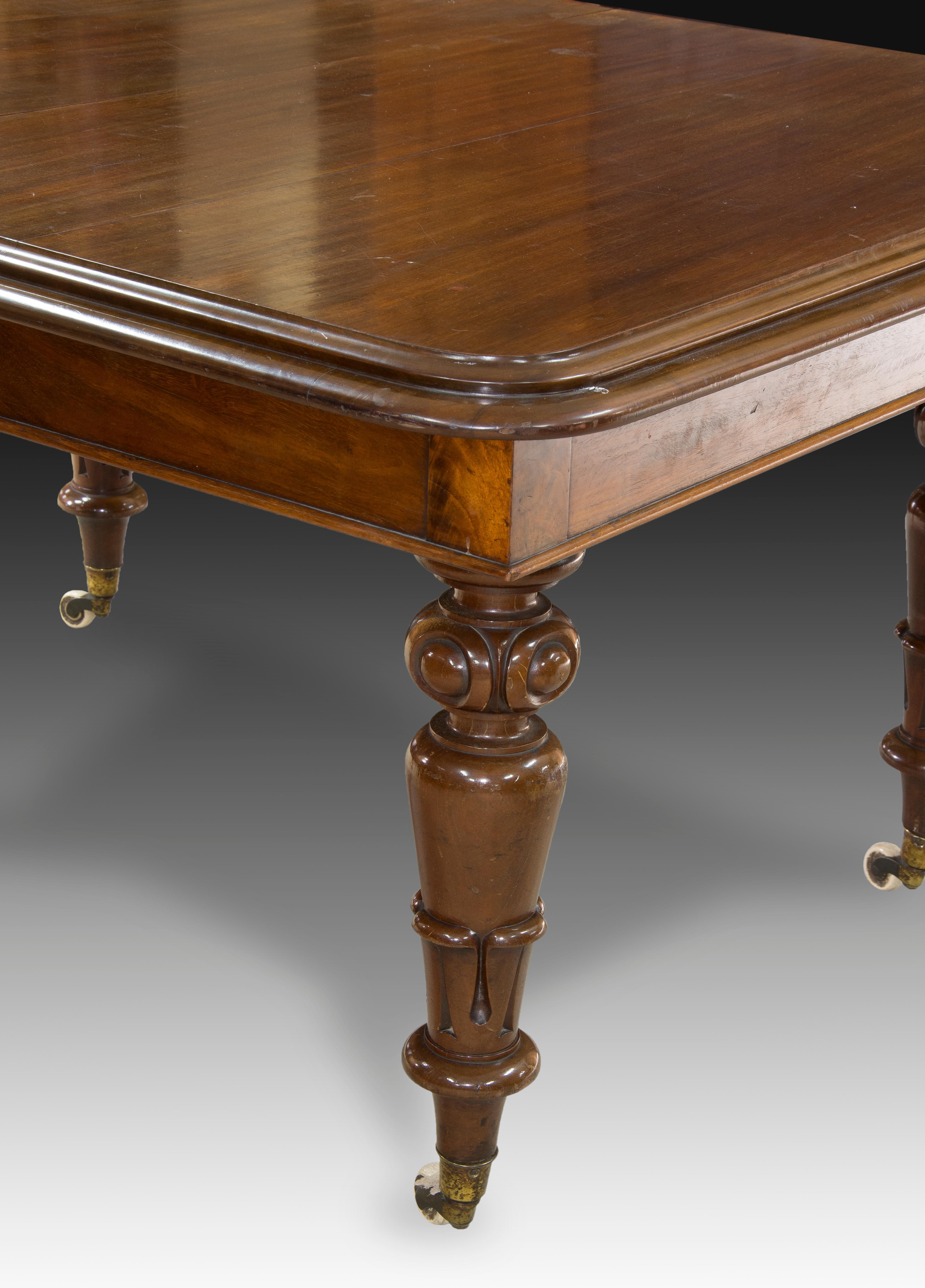 Extendable dining table. Mahogany wood. England, 19th century. 
 Rectangular dining table made of mahogany wood with metal rollers on the legs and a carving decoration concentrated on these supports, consisting of architectural and plant elements.