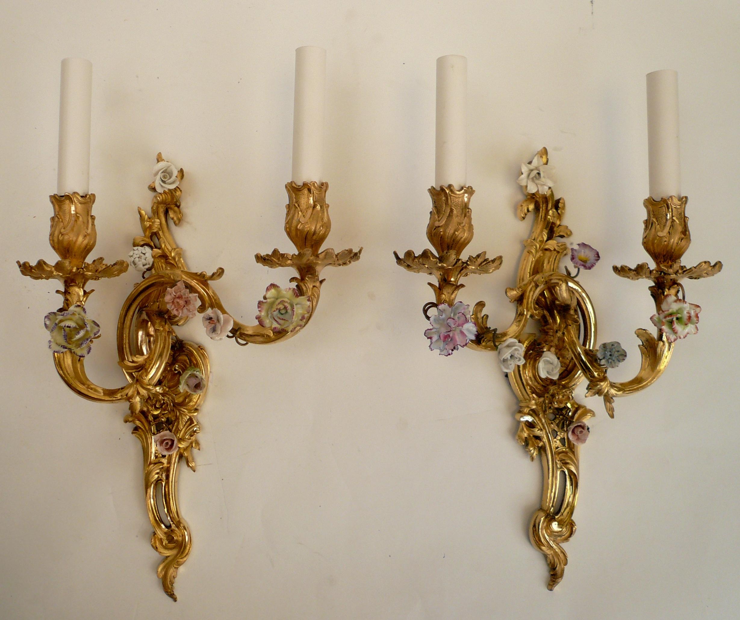 This beautiful pair of Louis XV style sconces are finely cast, hand chased, and burnished in gilt bronze. They feature scroll and foliate motifs, and are mounted with hand painted porcelain flowers.