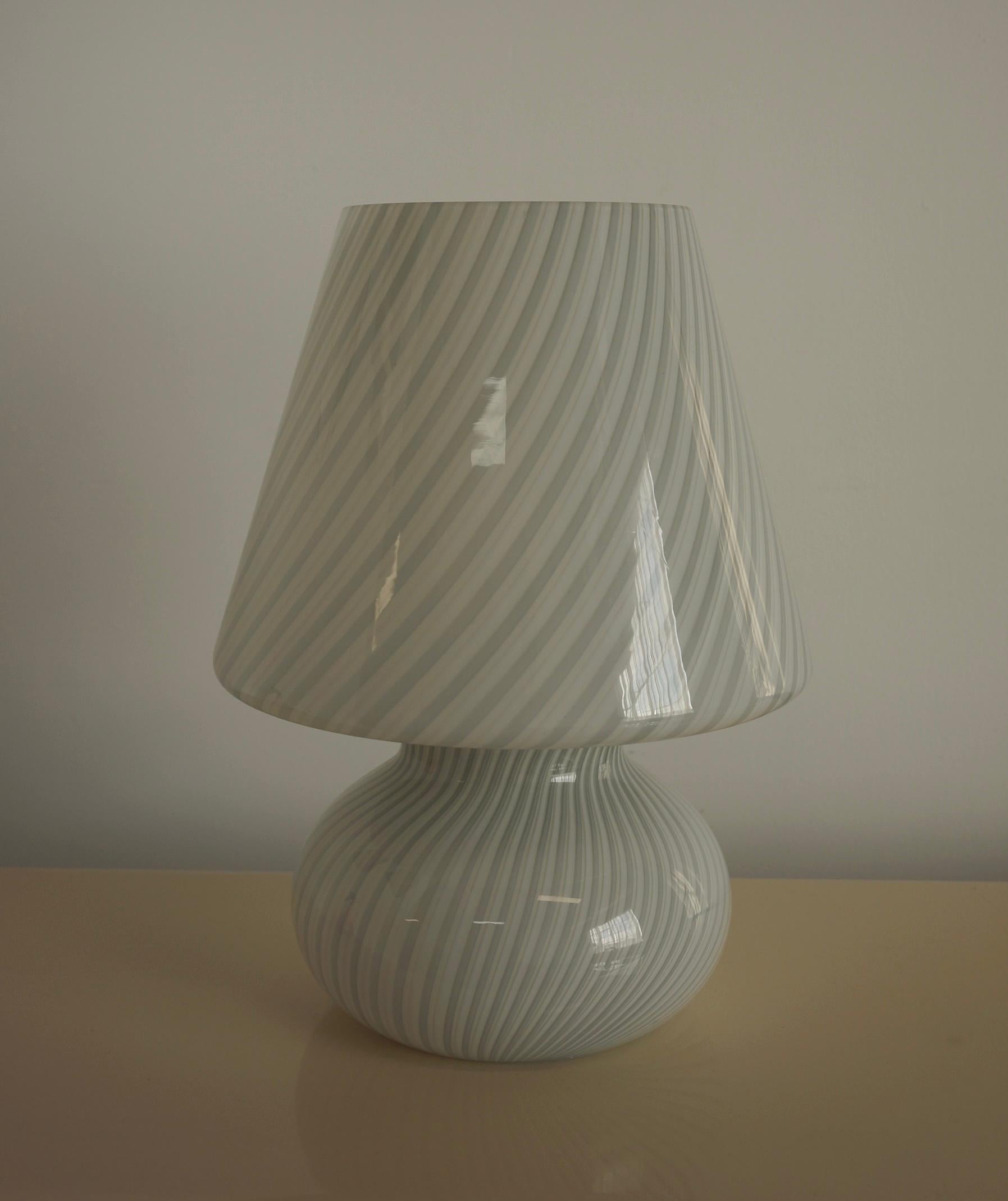 Lampe à champignon de Murano de très grande taille, réalisée selon la technique du tourbillon. Le tourbillon présente 2 couleurs de verre en gris et en blanc, joliment enroulées autour du verre blanc de base. Le verre d'art de Murano est considéré