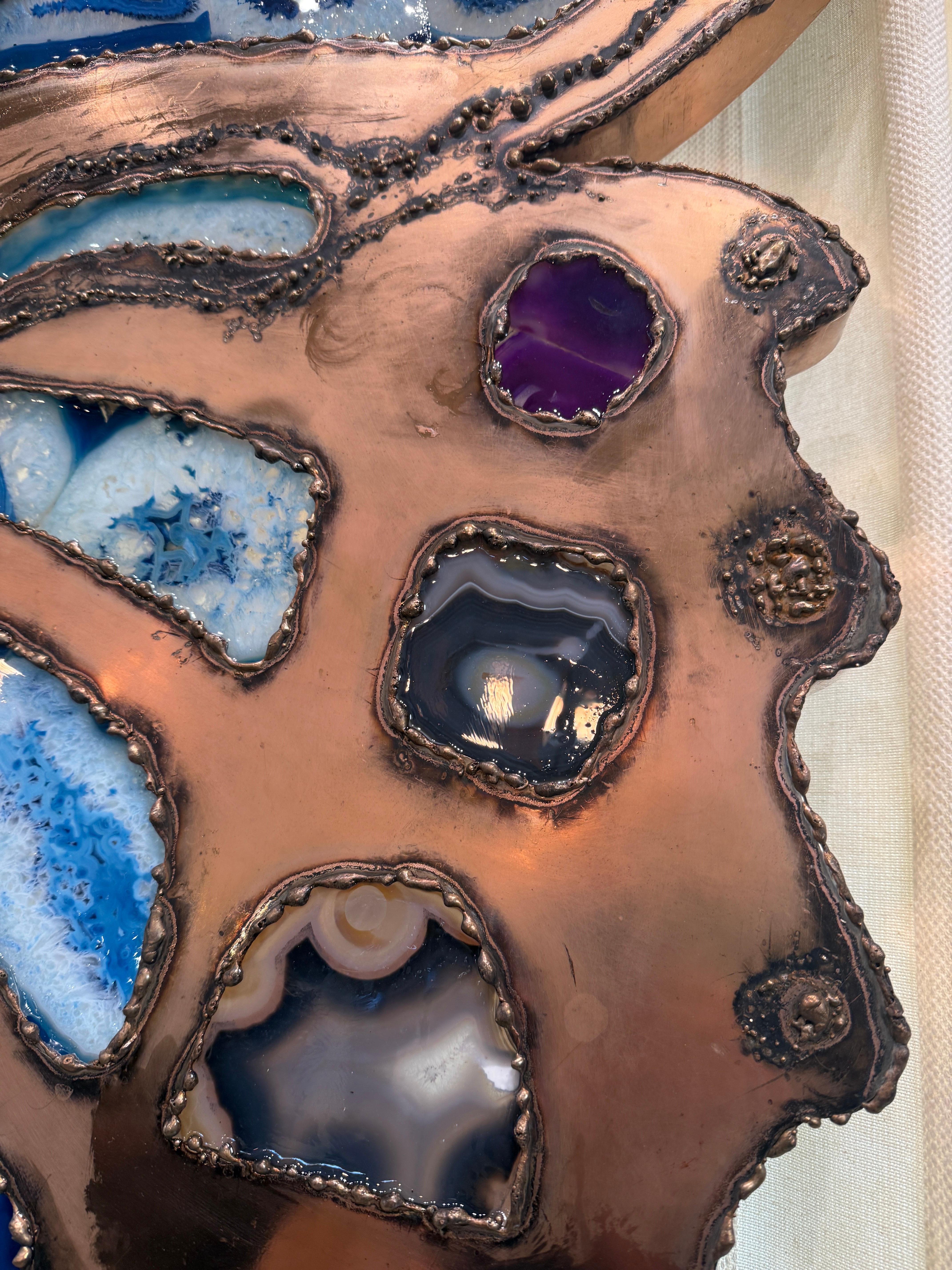 This 6 foot wide brass illuminating wall sculpture in a copper finish and adorned with multiple natural agate stones in blues, purple, ochre and grey.  This provides an outstanding lighting for any wall with back-lit ambient lights.  The agates come