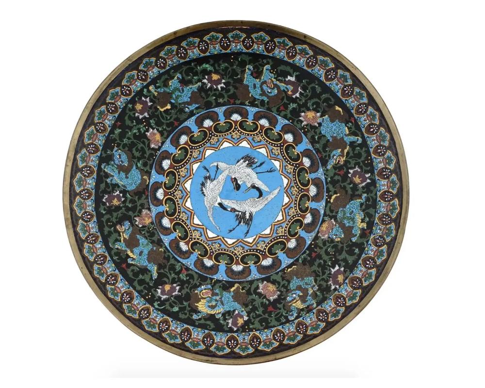 An extra large Japanese, early Meiji era, enamel over brass charger or plate. The plate is adorned with polychrome images of cranes surrounded by floral, foliage, geometrical, and scrollwork ornaments made in the Cloisonne technique. The borders are