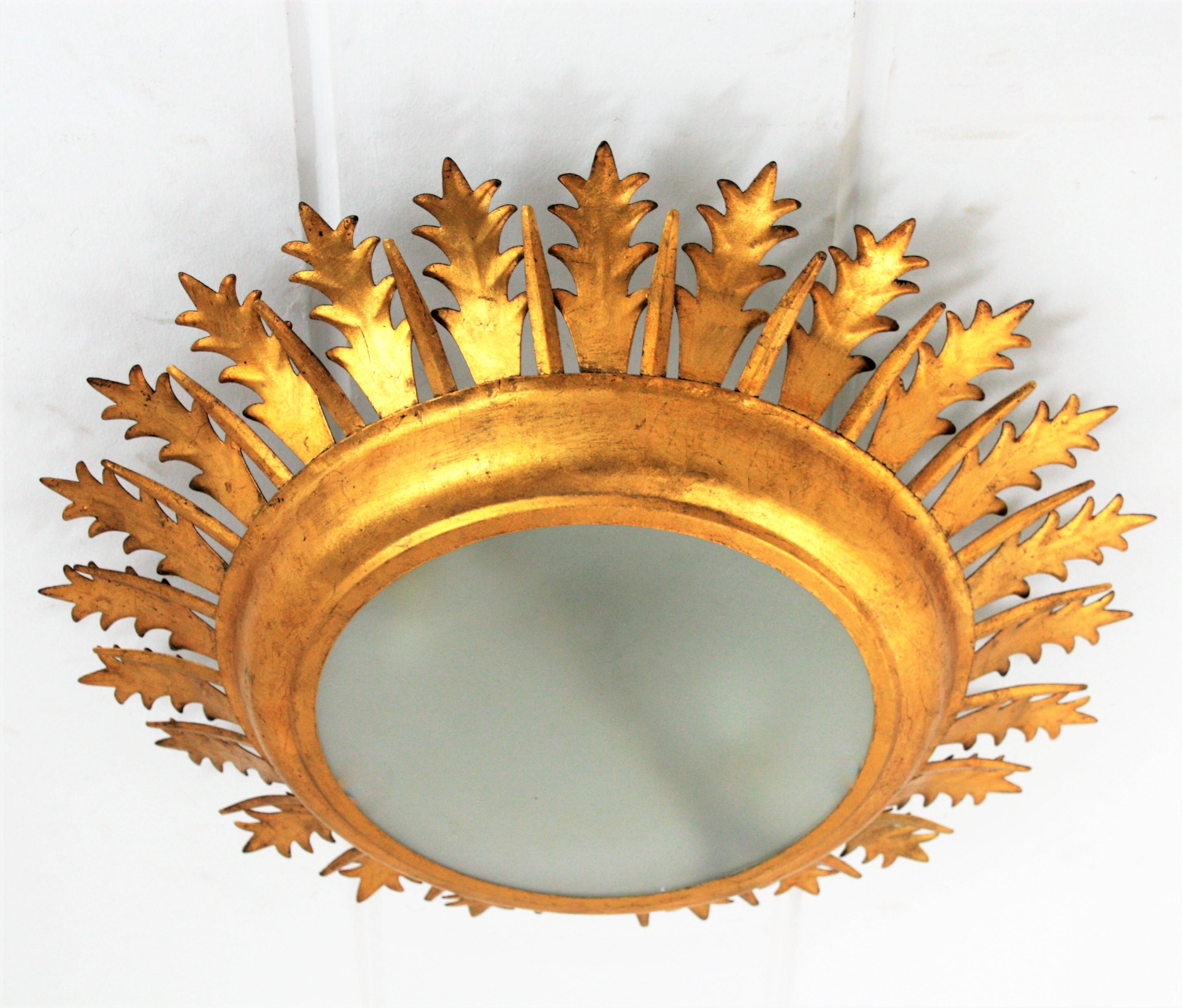 Extra large hand-hammered Mid-Century Modern gilt iron sunburst crown leafed light fixture with frosted glass difusser, Spain, 1950-1960.
This magnificent sunburst crown light fixture or flush mount has two layers of leaves in different sizes and