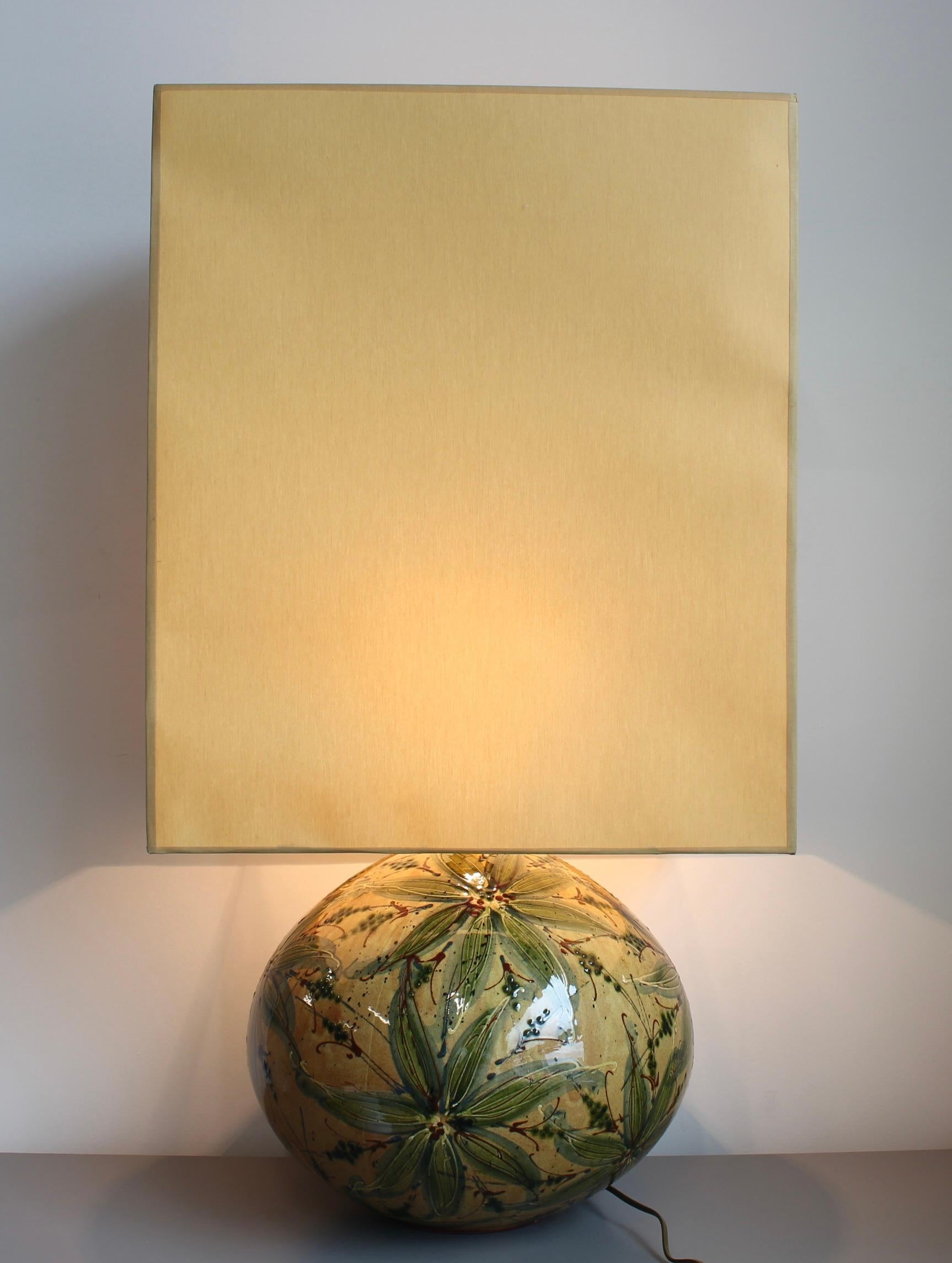 Cette lampe de table audacieuse et sculpturale en céramique des années 1980 présente une glaçure très brillante et un motif botanique richement peint à la main dans des verts olive, des bruns terreux et des ocres doux. La base généreuse et arrondie