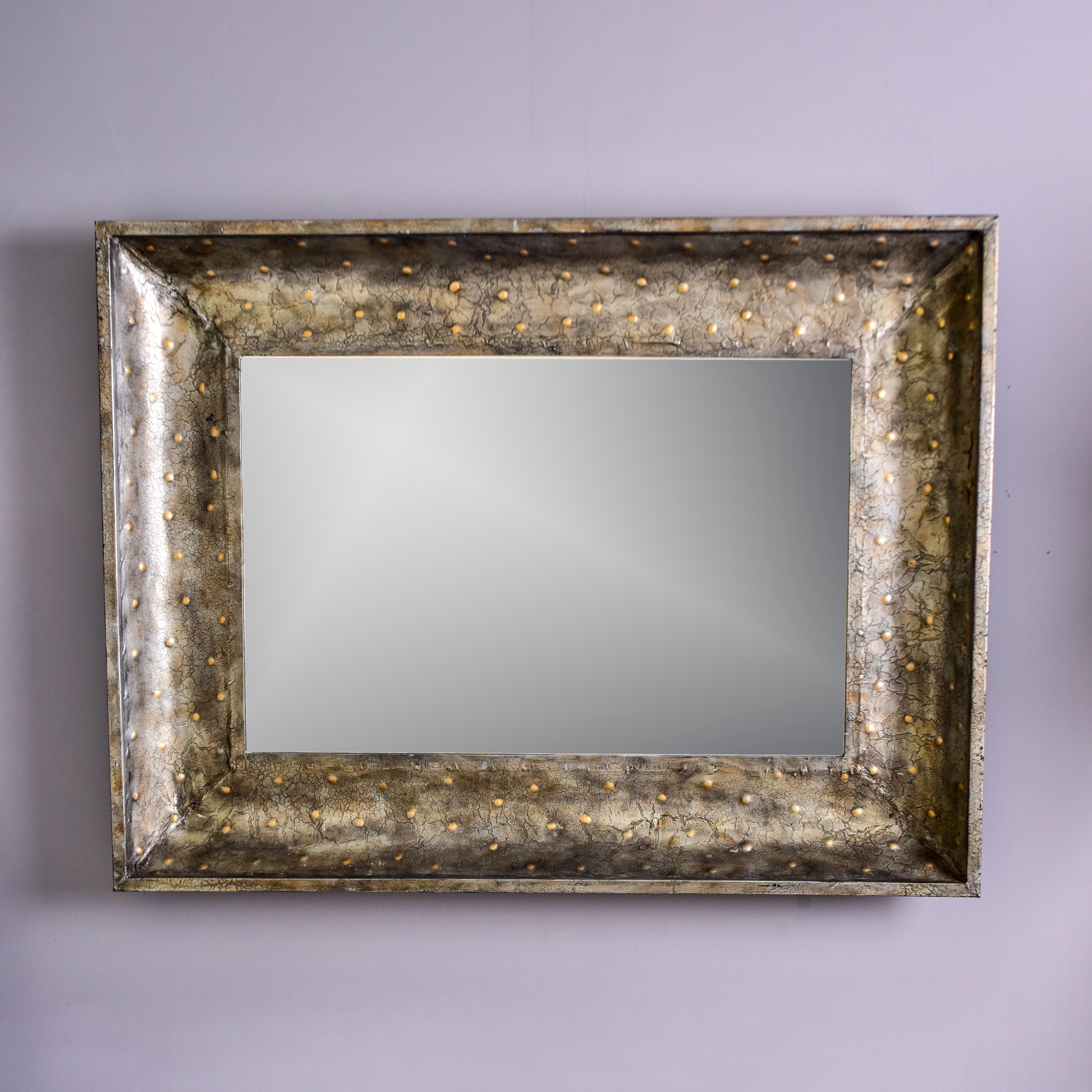 This large metal framed mirror can be hung vertically or horizontally and the longest side is just over five feet. The wide frame has a rustic, worn steel color finish with raised brass colored dots. Unknown maker. Found in the US.