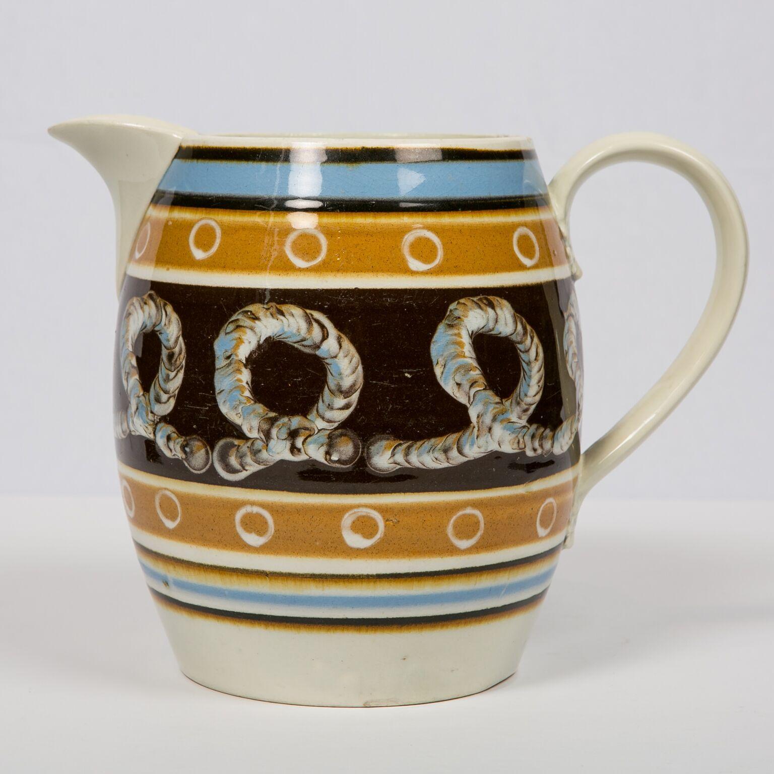 This wonderful pitcher is decorated with bands of light blue, and light and dark brown. In the band of dark brown is a three-color cable decoration. Small but important detail on this pitcher is the rare decoration of white offset circle design. The