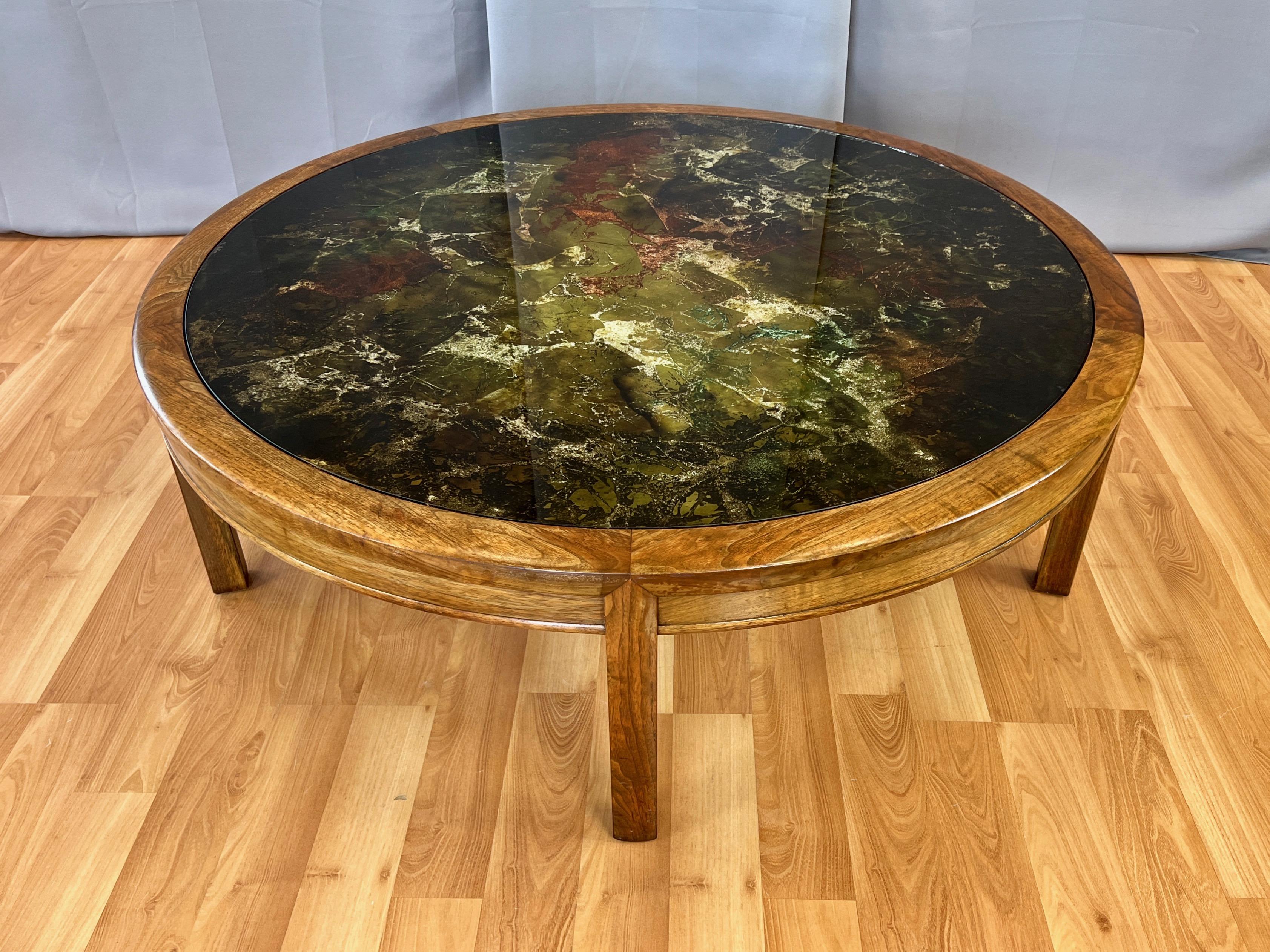 An impressively sized and uncommon late 1960s four-foot-diameter round walnut coffee table with striking abstract metal leaf and hand-painted verre églomisé top.

Expansive glass top features an absolutely dynamic design on its underside comprised