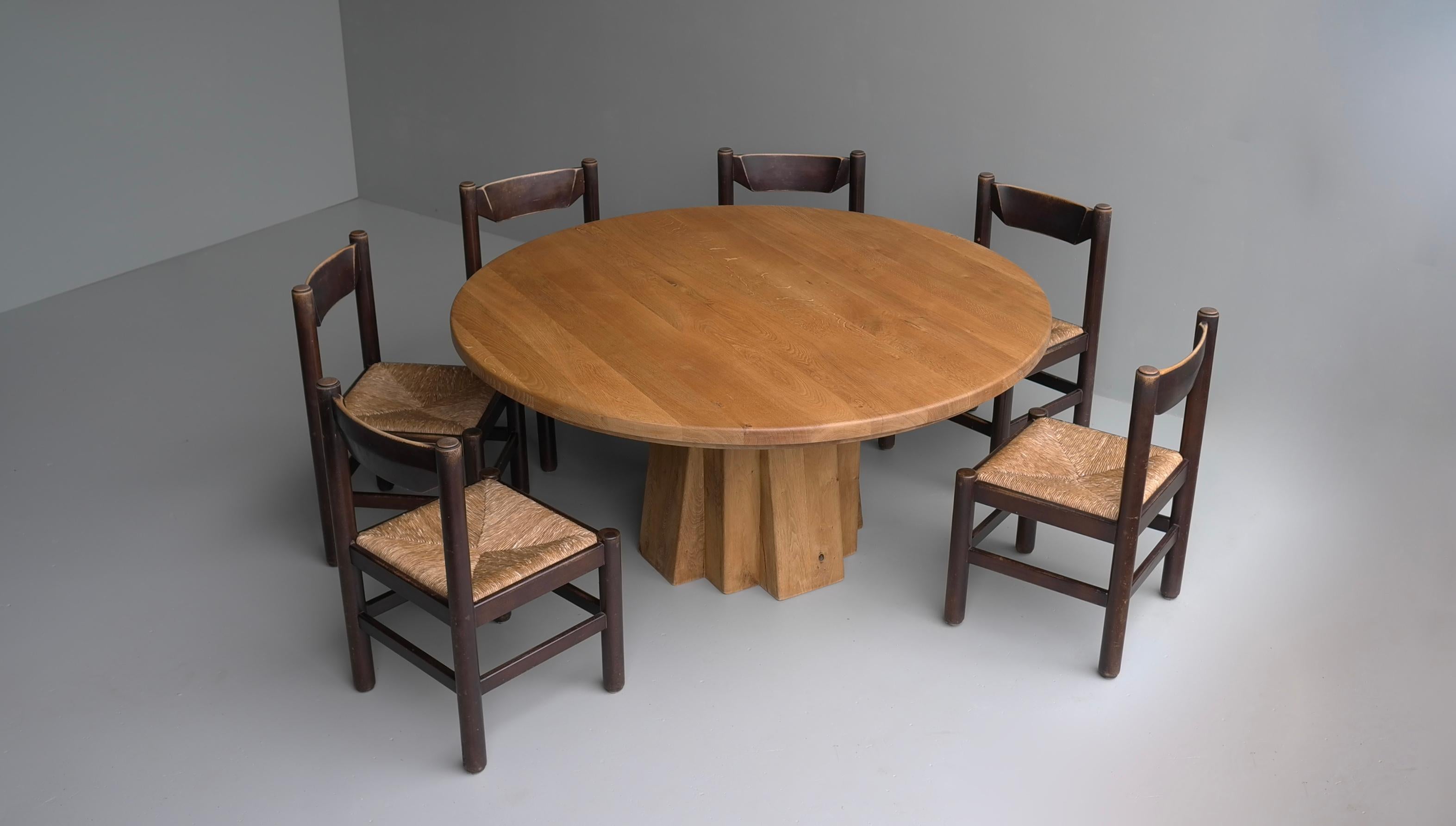 This very large round table is made from solid oak with a unique sculptural carved base. Very Heavy and solid piece. The chairs are made from solid wood, heavy and robust with rush seats. These chairs have a fine patina with marks of usage and they