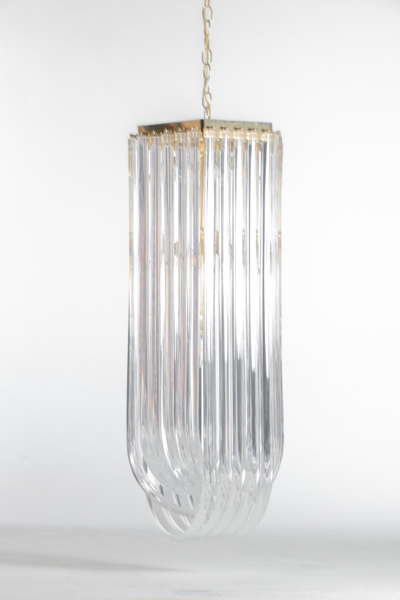 Lucite ribbon chandelier with brass frame. Sculptural interlocking ribbons of Lucite hang from a brass frame, circa 1970s. The fixture would be a statement piece in an entryway or stairwell, or any room with high ceilings. Want to see more beautiful