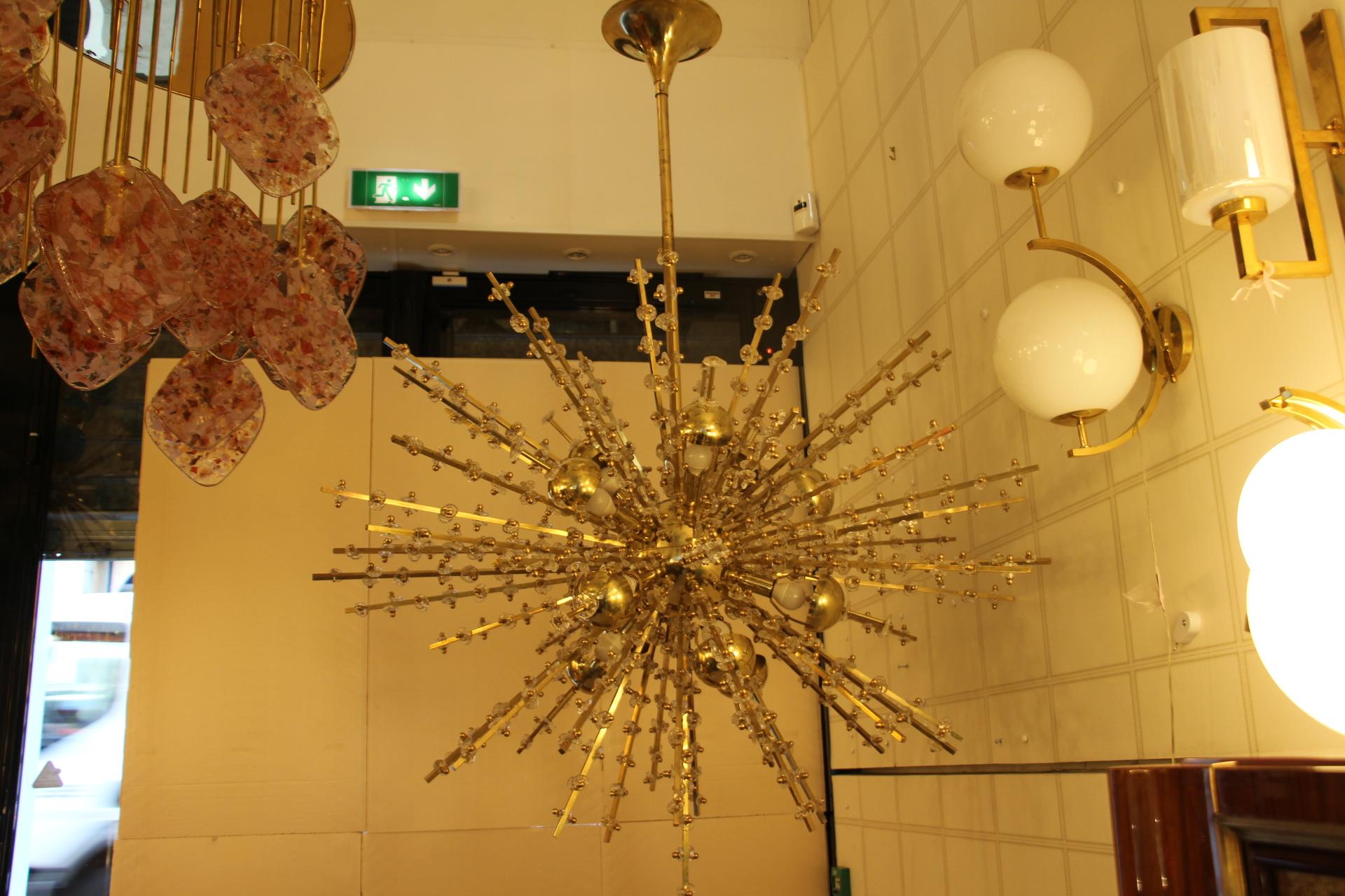 This spectacular sputnik looks like a sunburst explosion.It features a multitude of brass rods of different length. Each rod is directly fixed on its polished brass central sphere.Its rods are sprinkled with delicate clear Murano flowers and give to