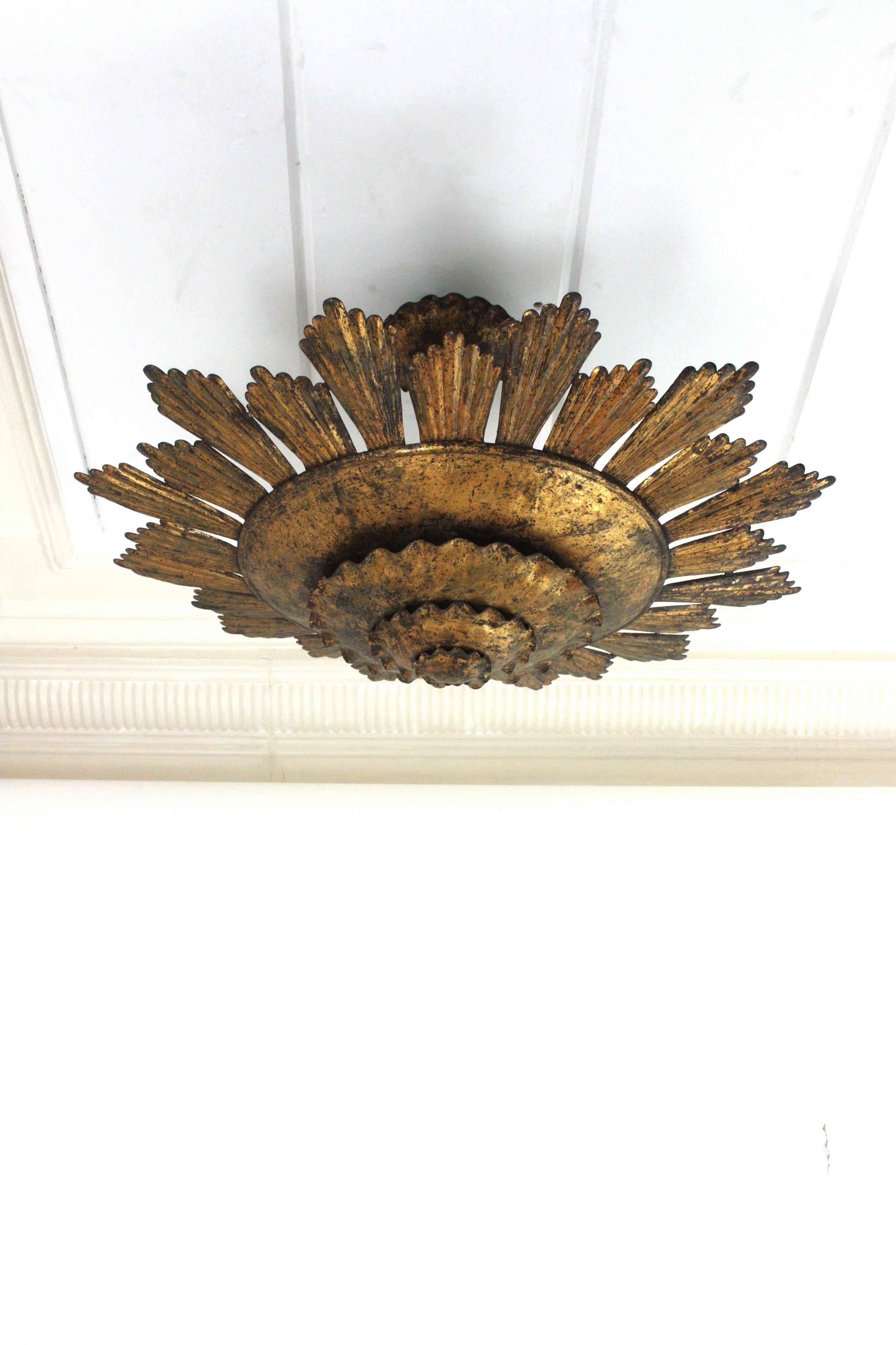 Luminaire unique en son genre, de très grande taille (31,5 pouces), en forme de soleil doré, en fer forgé. Espagne, années 1940.
Ce monumental encastré de plafond à trois couches a été entièrement fabriqué en fer forgé à la main et terminé par une